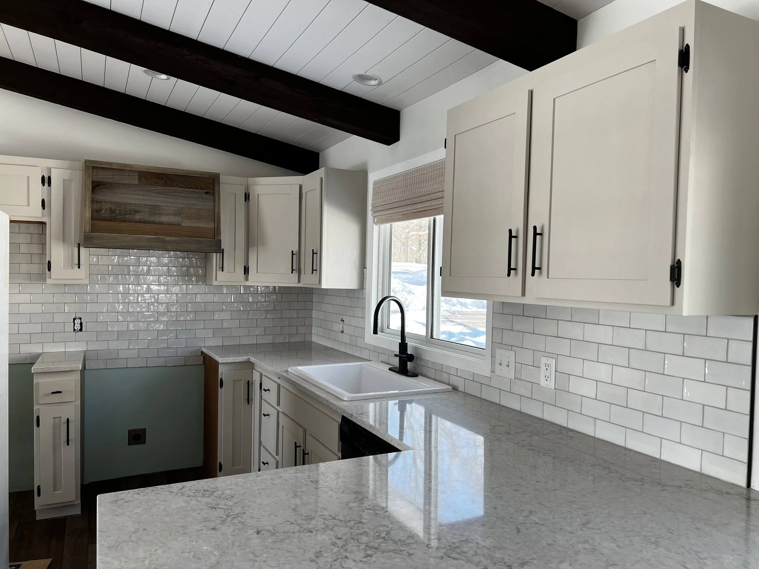 Modern kitchen with white cabinets, a white subway tile backsplash, black hardware, a black faucet, and a window with a view of snow outside.