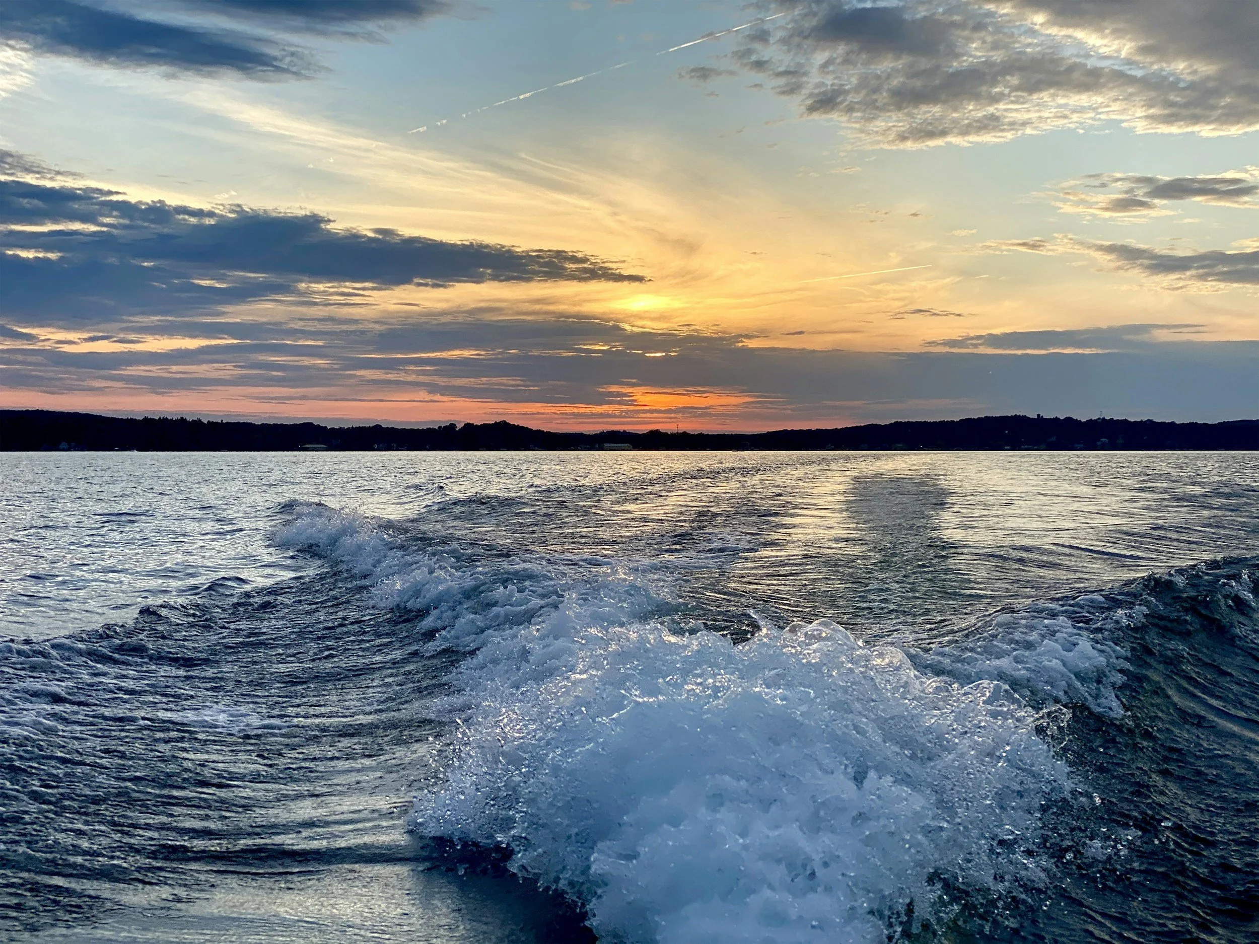 Sunset over a lake with a boat wake in the foreground.