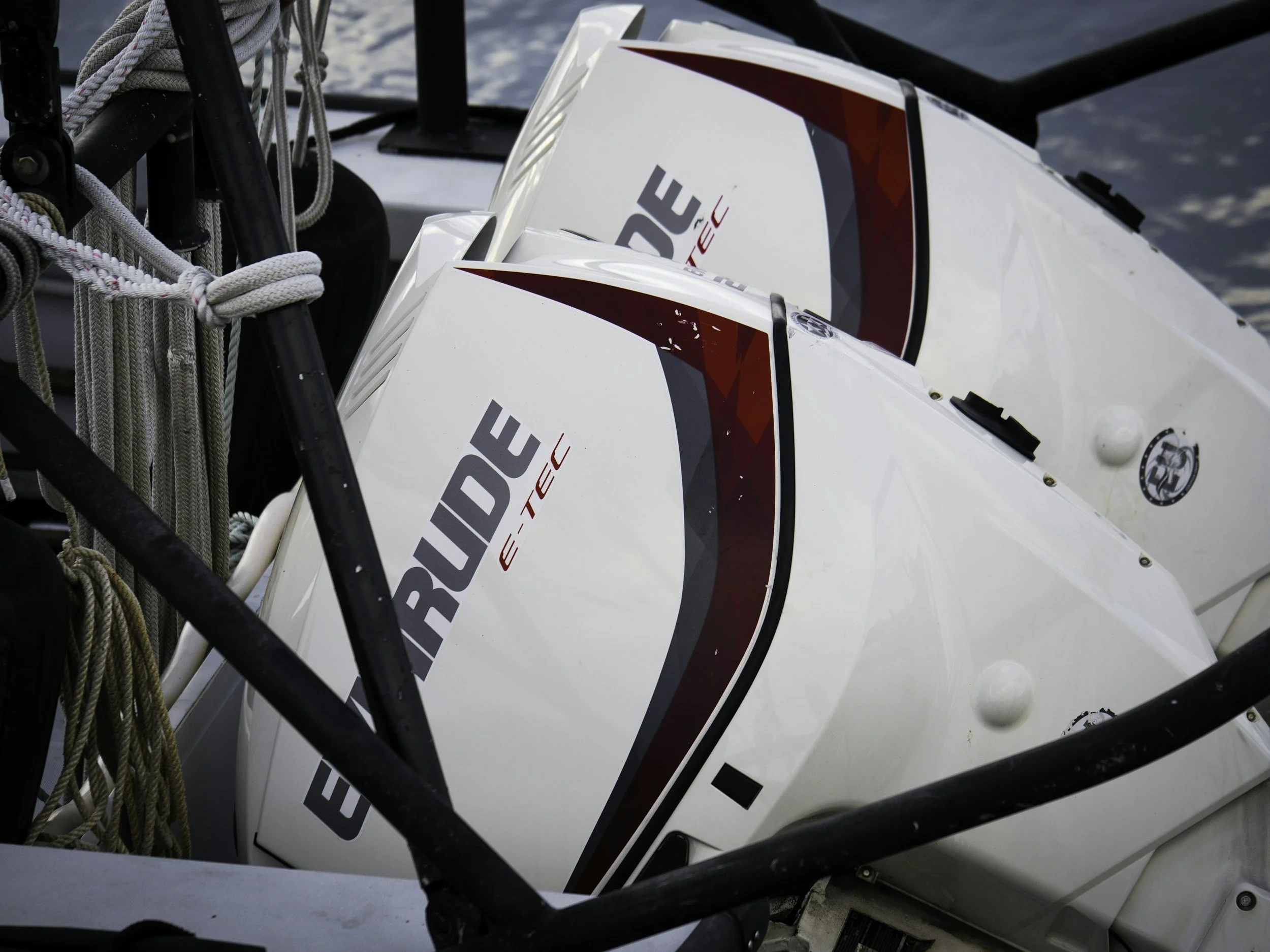 Two white E-TEC outboard motors mounted on a boat with ropes and safety rails nearby.