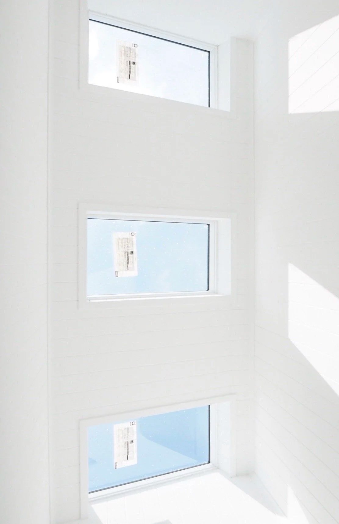 Three rectangular windows on a white wall, with sunlight creating shadow patterns.