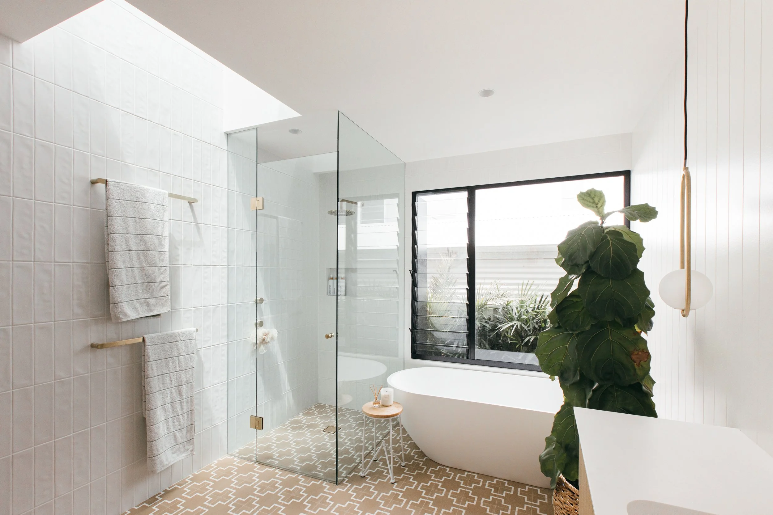 Modern bathroom with a glass shower, white bathtub, large window, potted plant, and minimal decor.