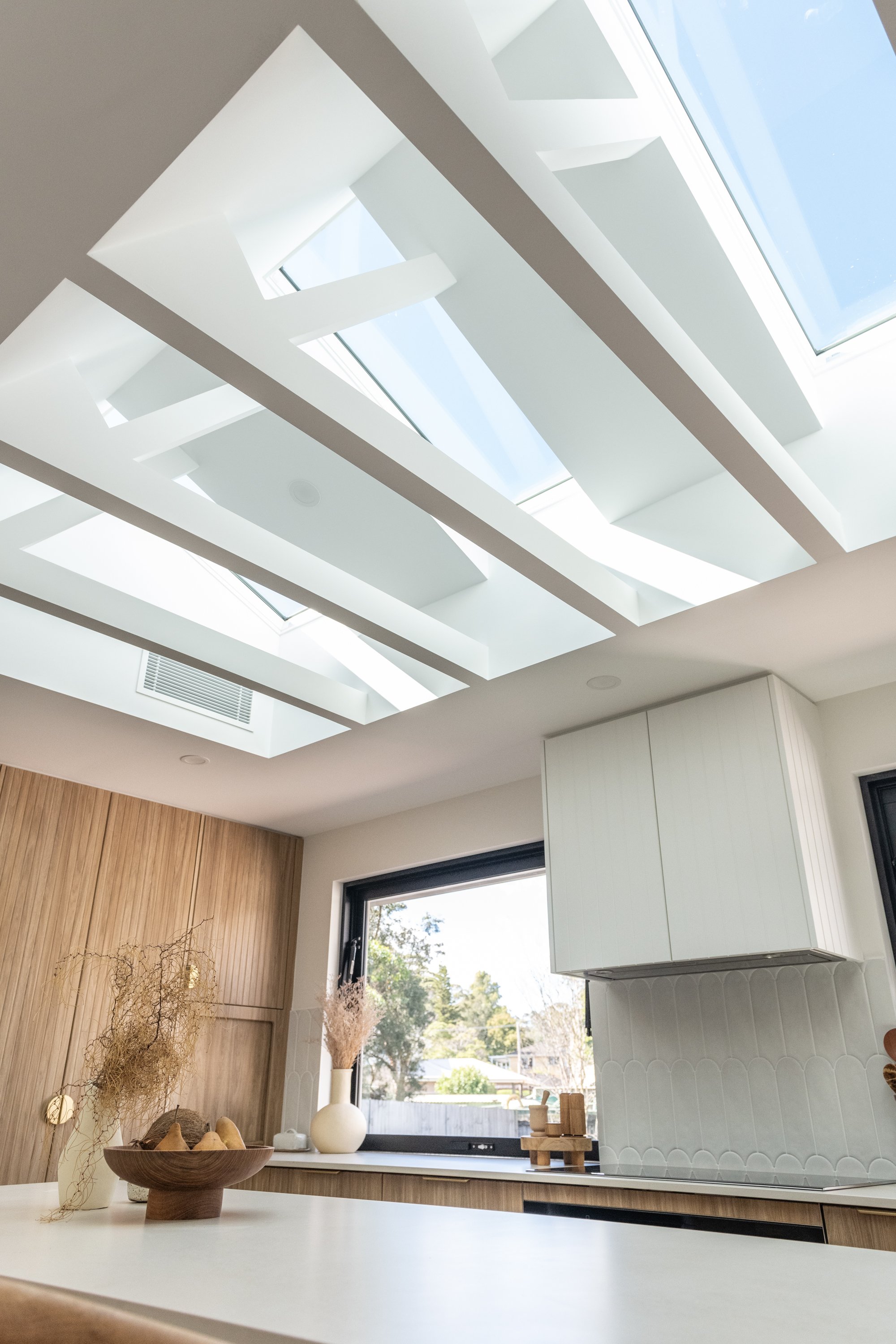 Modern kitchen with a white countertop, wooden accents, decorative vases, and a ceiling with skylights.