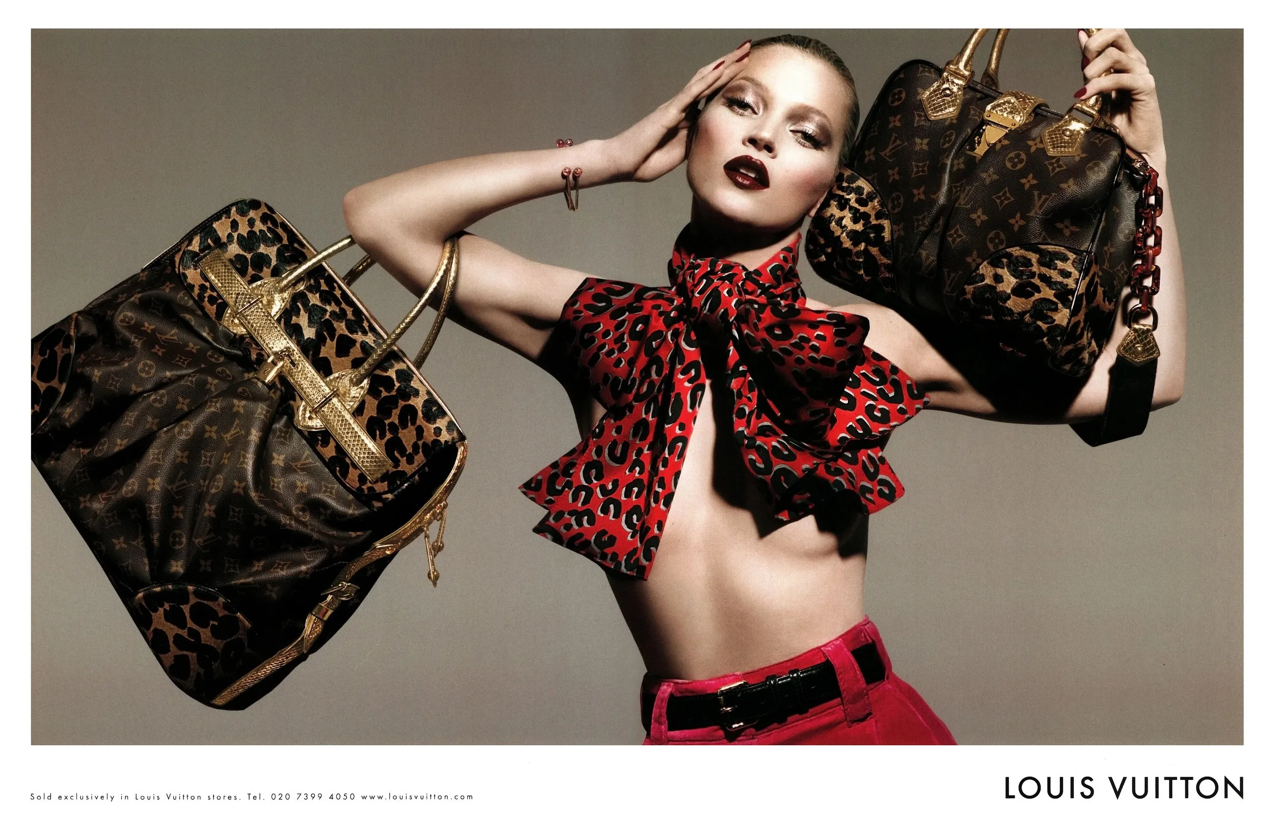 A woman with fair skin, wearing a red leopard print top tied around her neck, red pants with a black belt, gold jewelry, and dark lipstick, is holding two large Louis Vuitton handbags with leopard and monogram patterns over her shoulders and head.