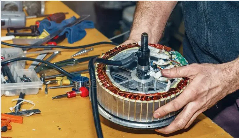 Person repairing or assembling a circular electric motor or generator on a workbench surrounded by various tools and parts.