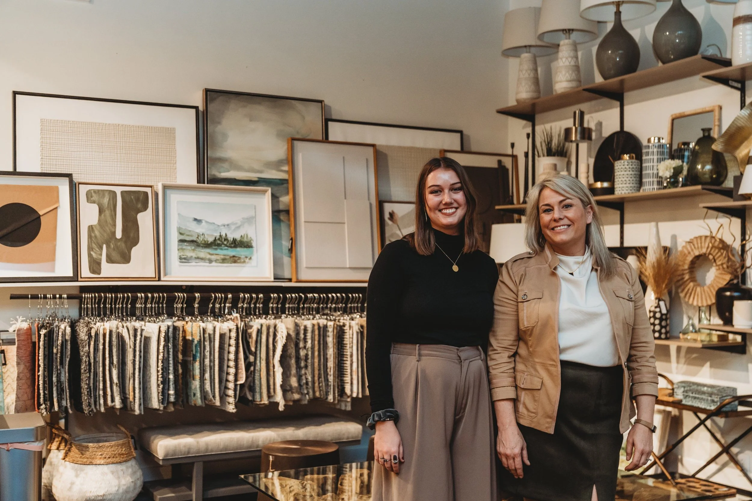 Two women smiling in a home decor store with artwork and vases on display.