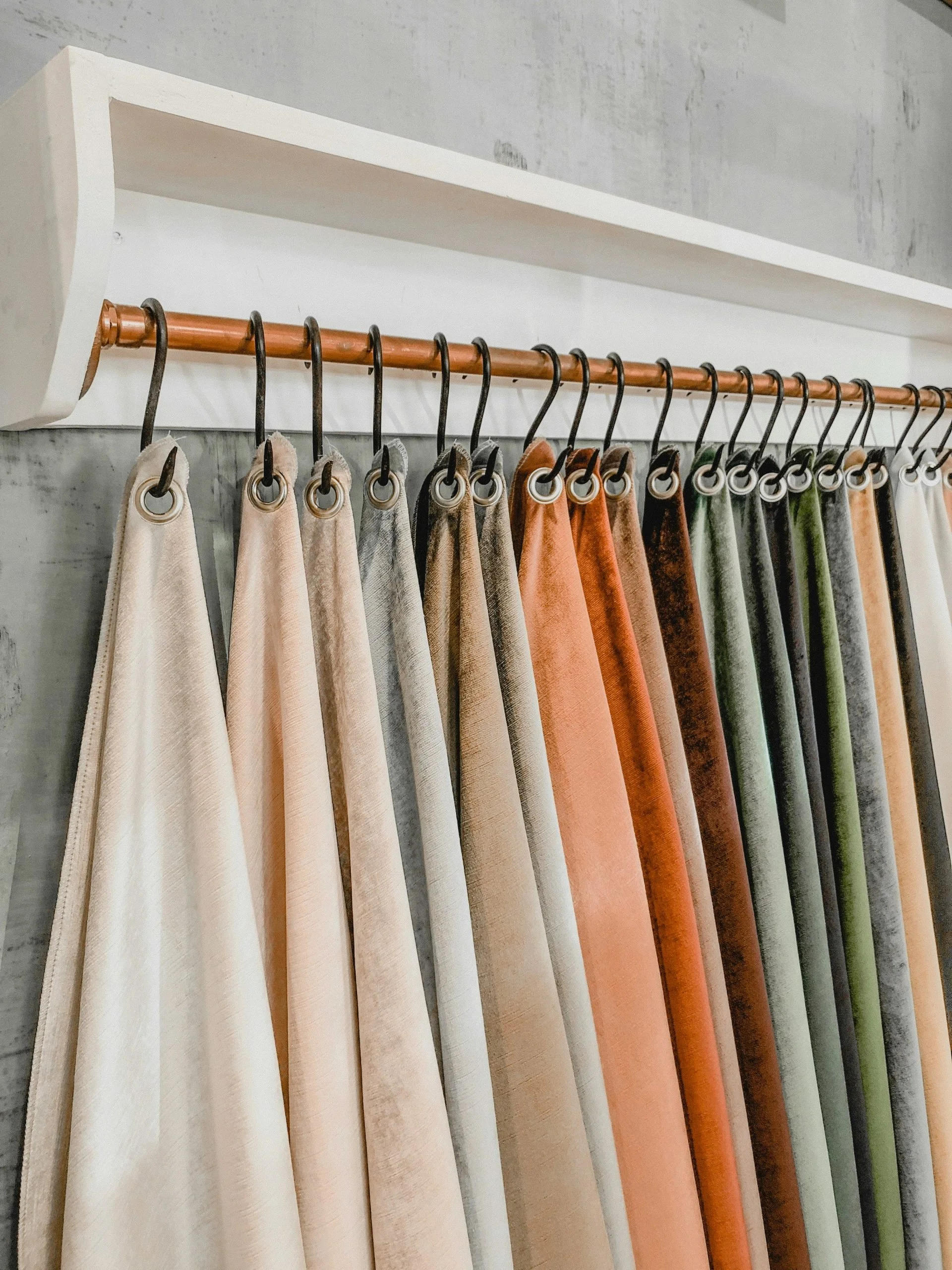 Rows of velvet curtains in various colors hanging from a rod in a showroom or store.