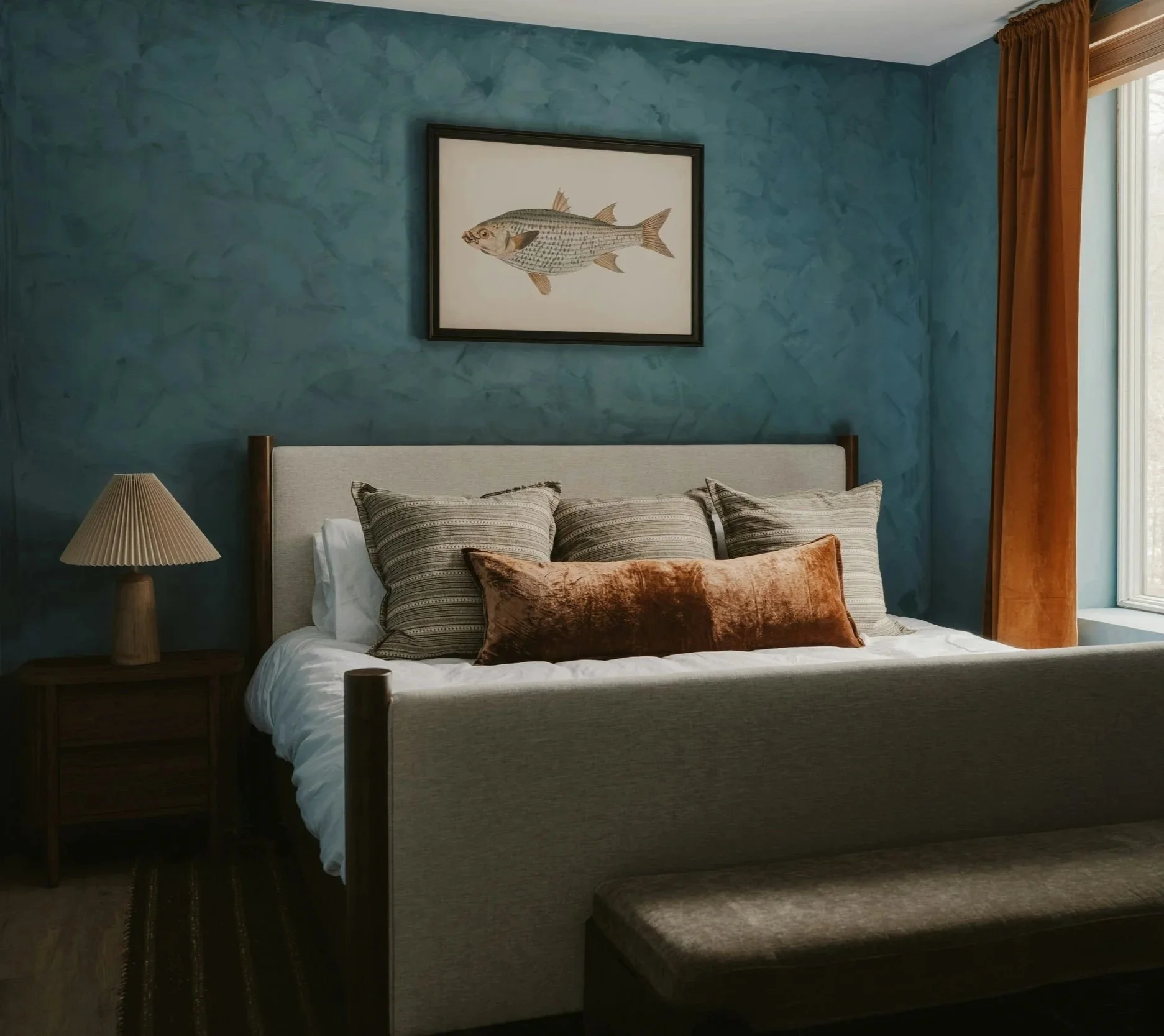 Textured blue limewash accent wall behind a bed with layered neutral textiles.