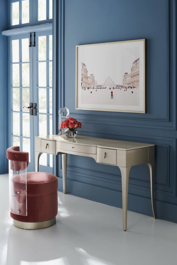 Hollywood Glam home office featuring a curved ivory writing desk, blush velvet accent chair with acrylic detailing, blue paneled walls, framed artwork, and fresh floral accents, creating a sophisticated and elegant workspace.