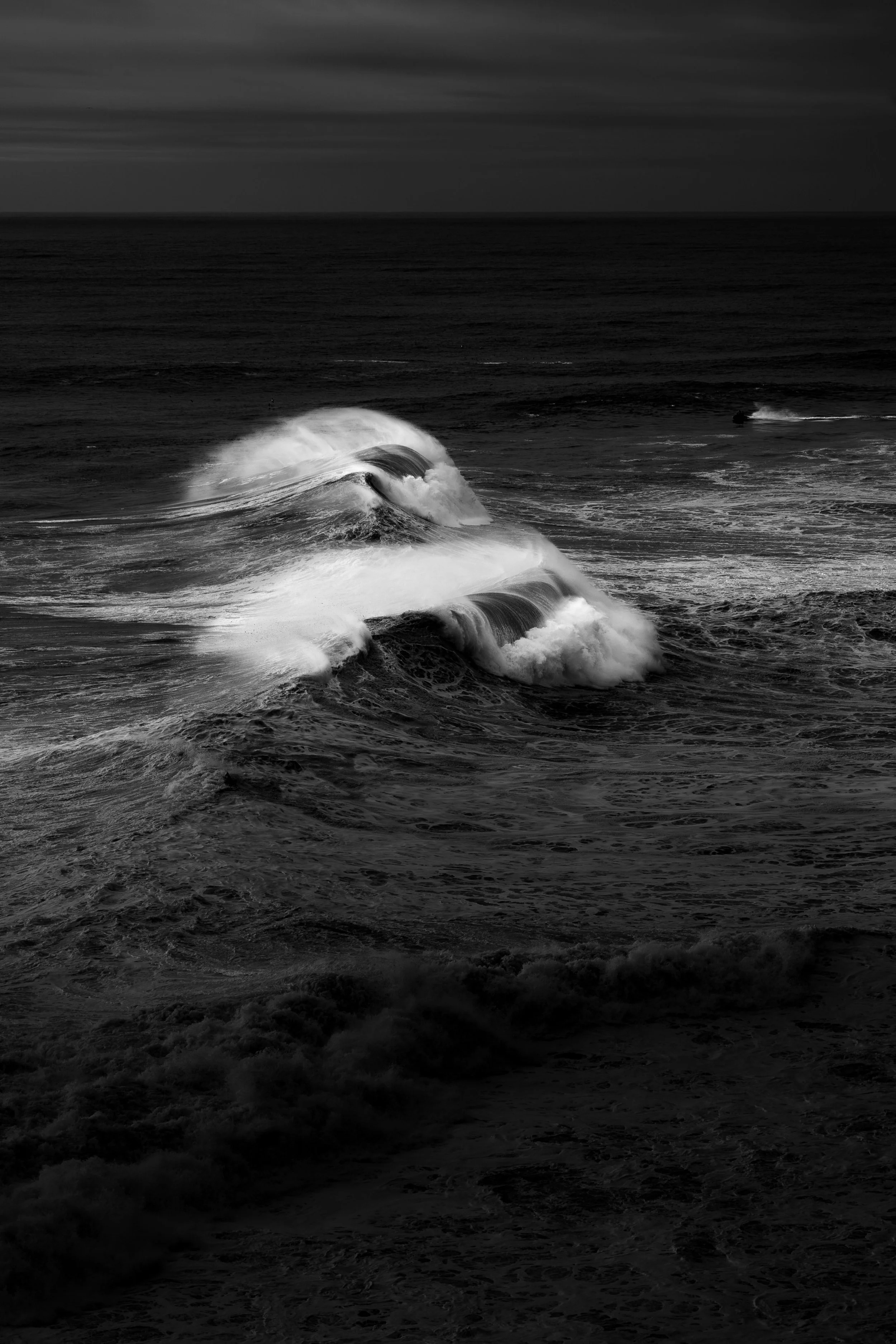 Black and white photograph of ocean waves crashing against each other with a cloudy sky above.