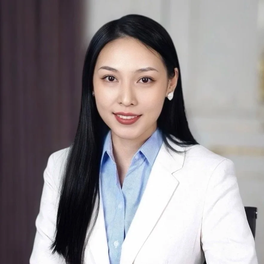 A young woman with long black hair, wearing a white blazer and blue shirt, smiling at the camera.