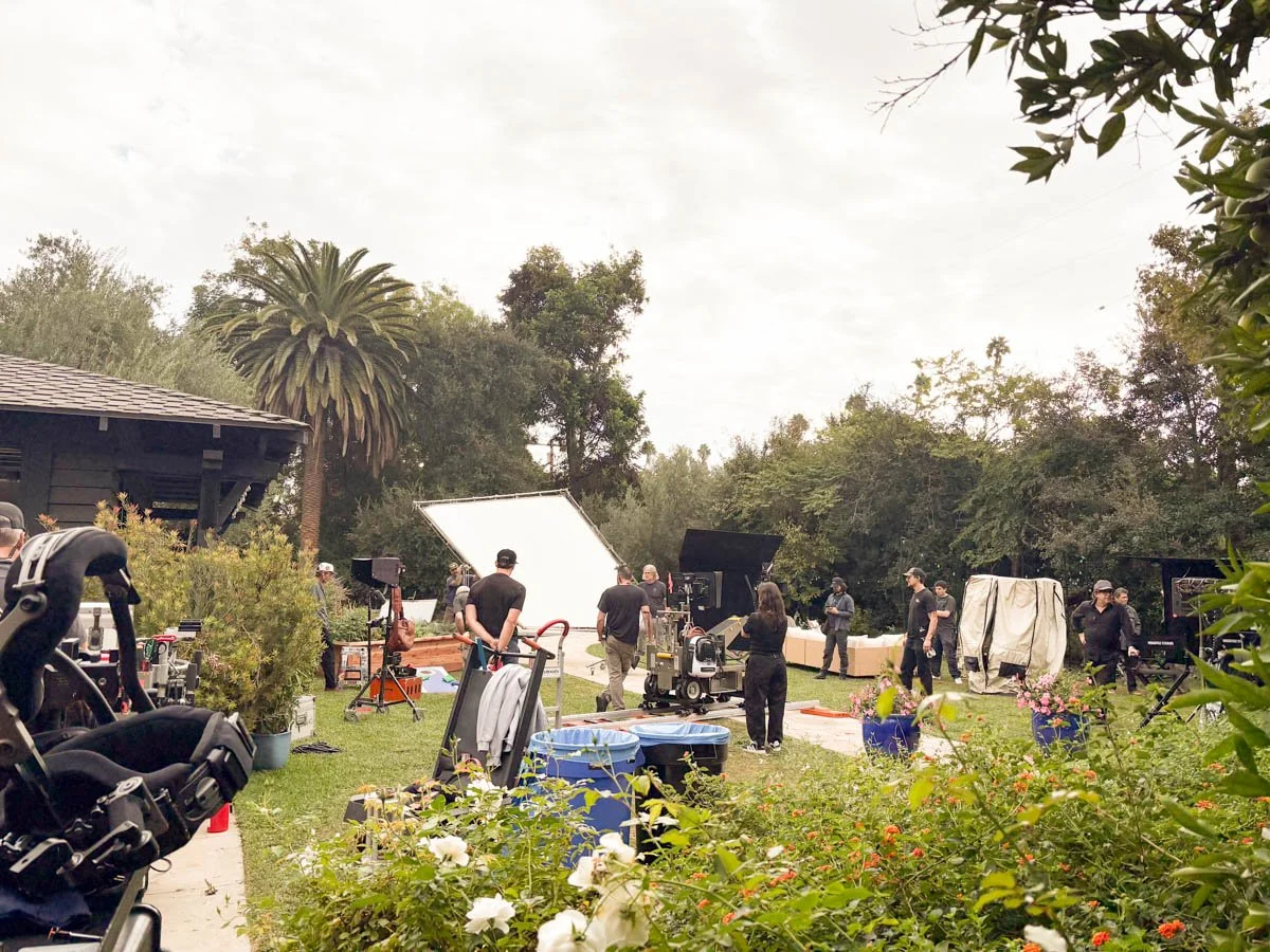 Filming crew on a lush green lawn with professional equipment, large reflectors, and crew members preparing for a shoot outdoors.