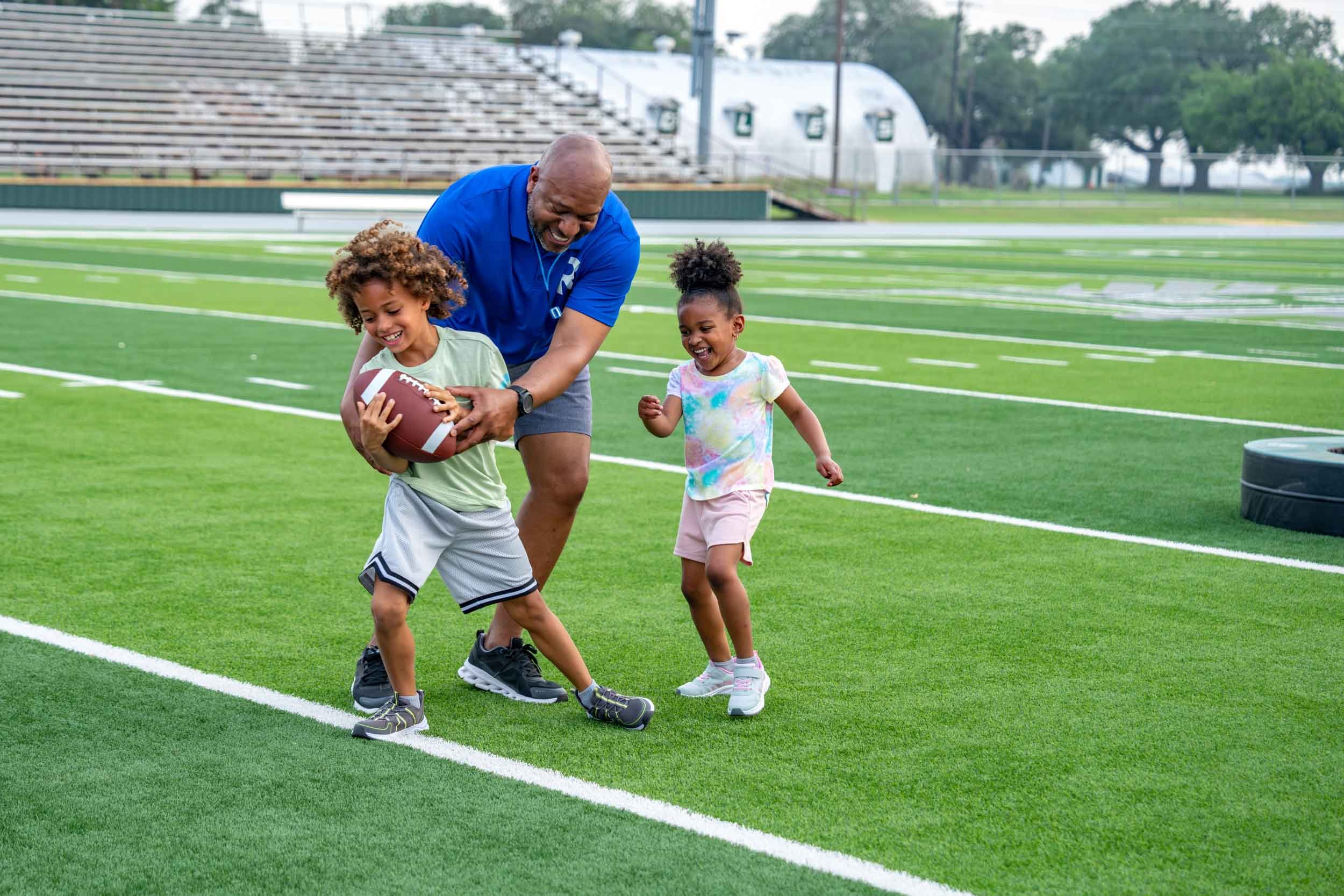 Man-Playing-Football-with-Kids-on-Sports-Field.jpg