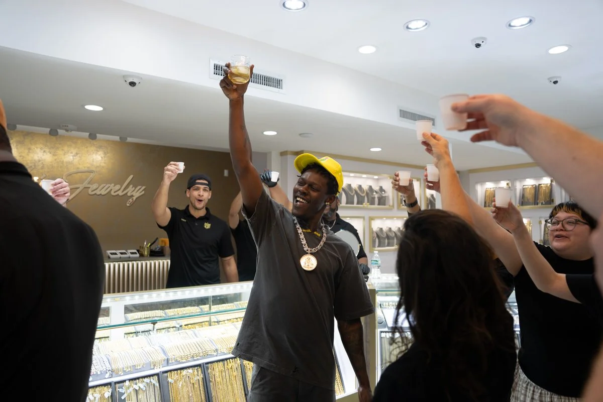Group of people celebrating together, raising glasses of champagne or wine in a jewelry store with display cases of jewelry and a sign that says "Jewelry" in the background.