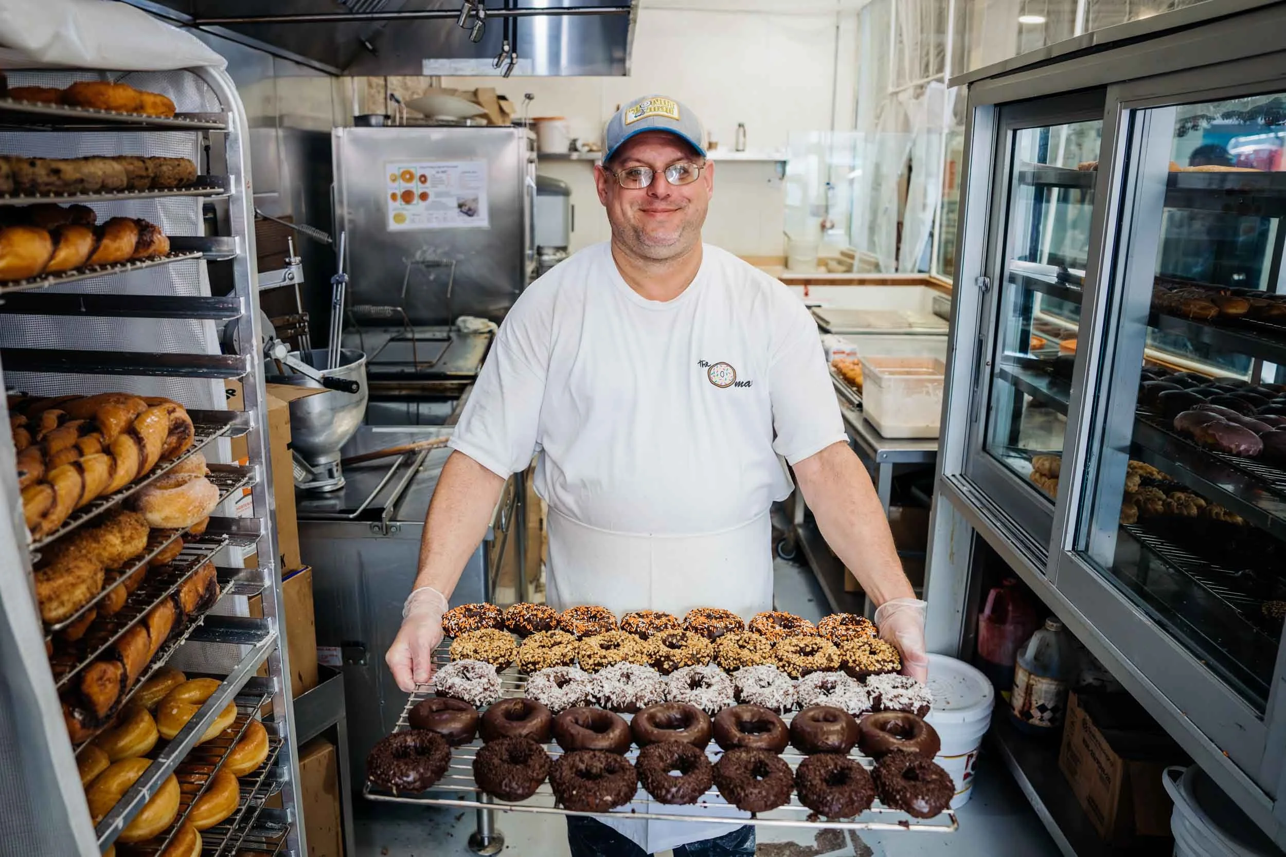 Man-Holding-Tray-of-Doughnuts-in-Bakery.jpg
