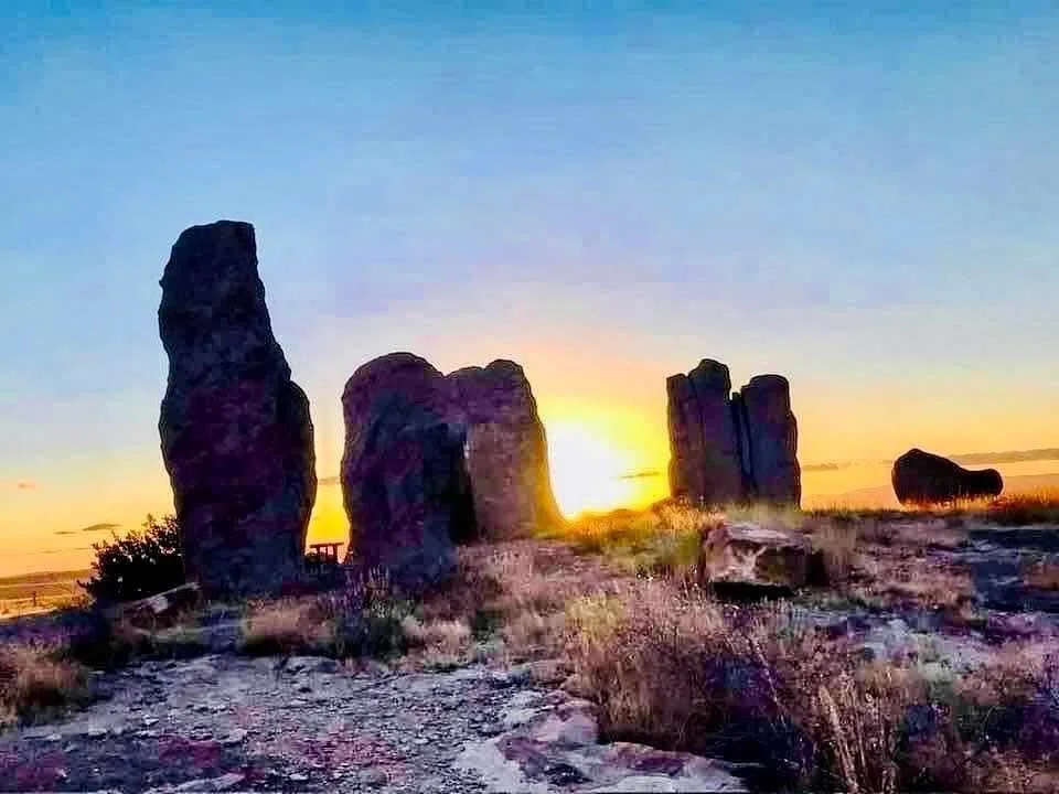 Sunset behind large ancient stone formations in a dry grassy landscape.