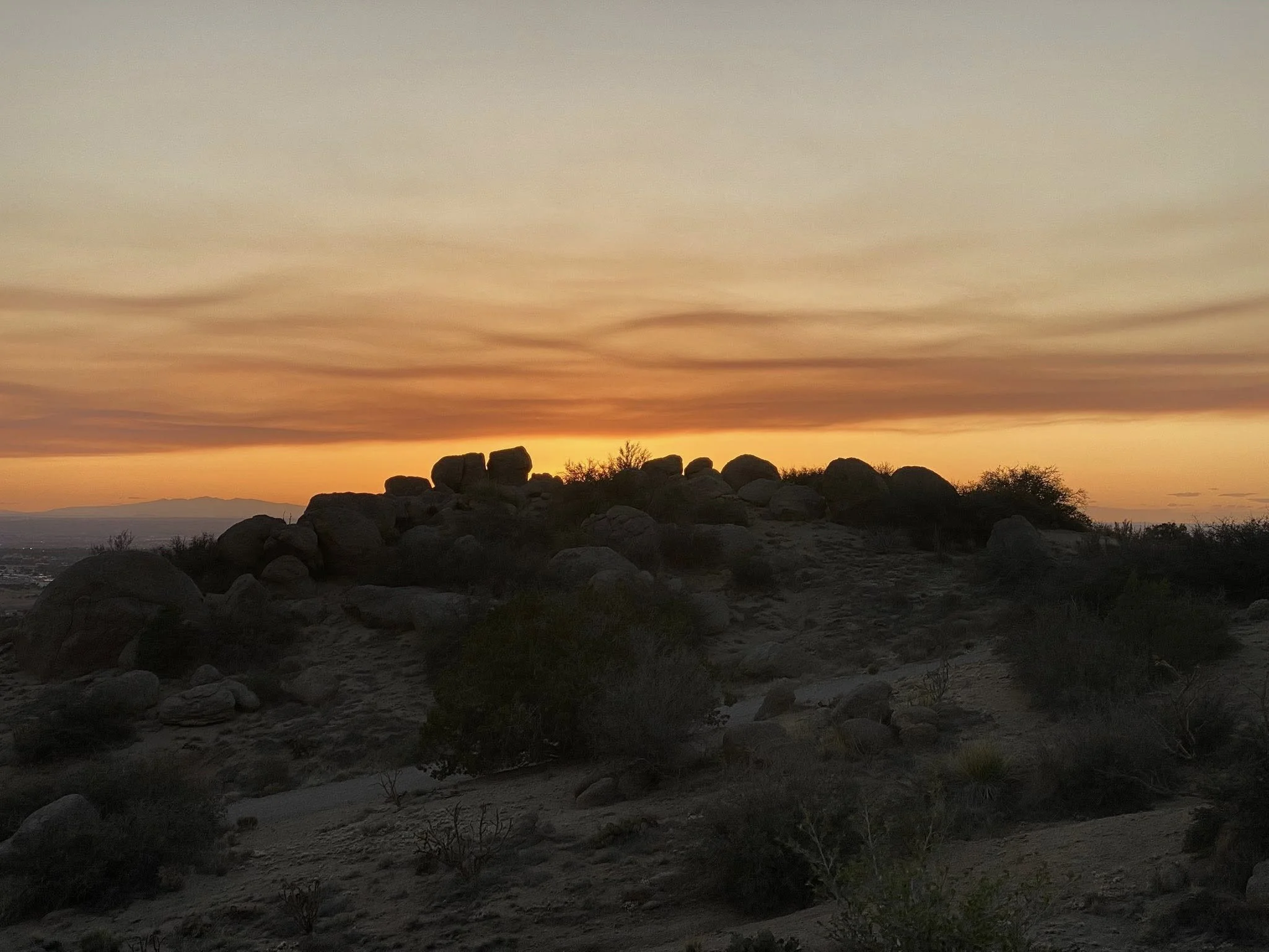 Sunset over a rocky desert landscape with sparse desert vegetation.