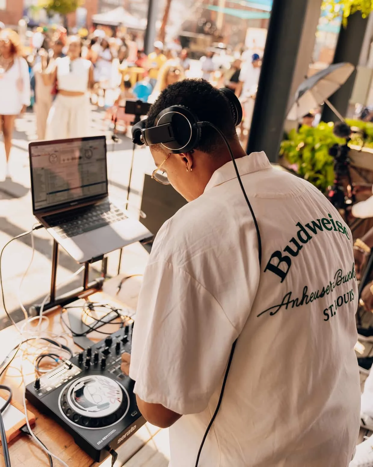 DJ playing music at an outdoor event with crowd in the background.