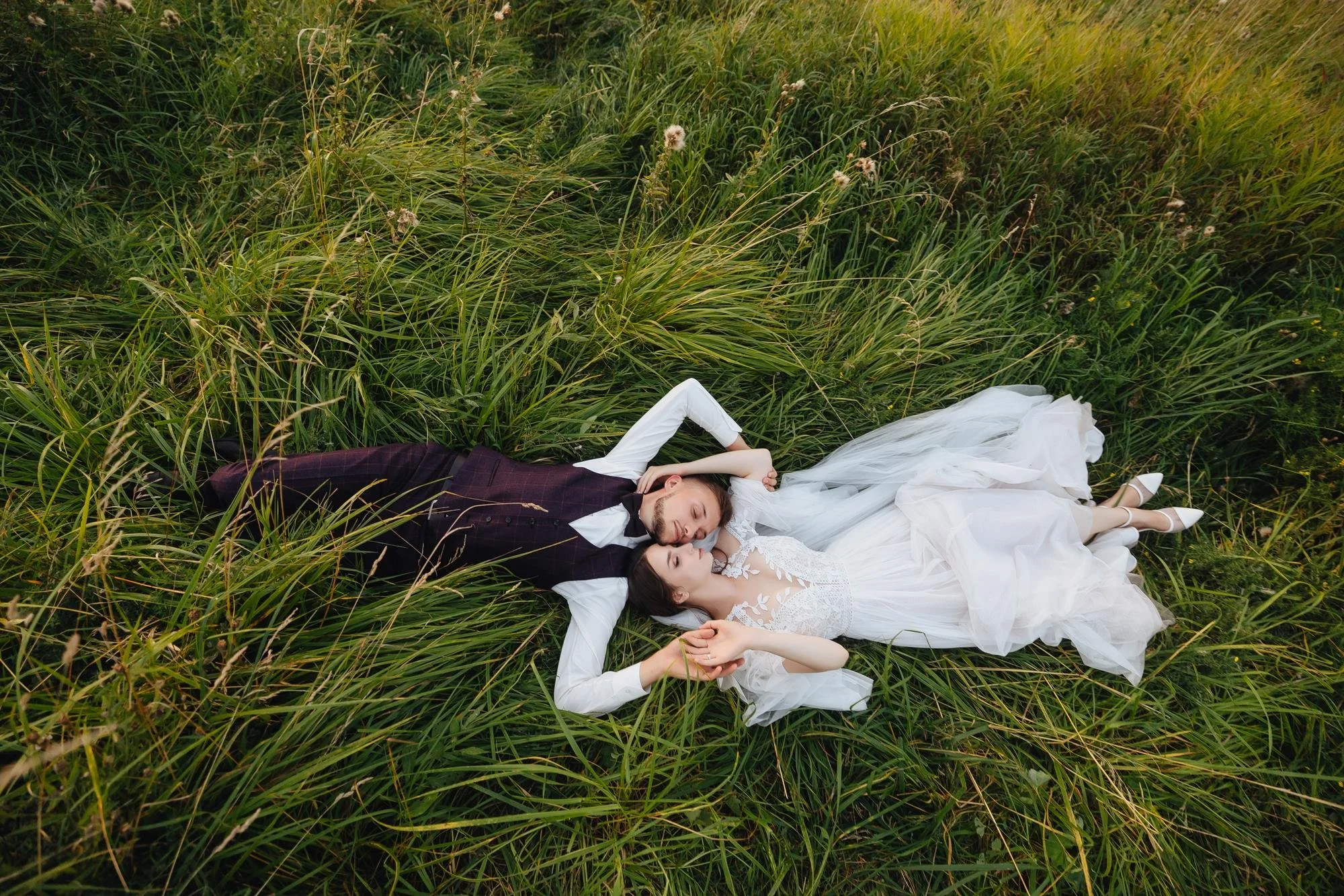 Ein Paar liegt in einem hohen Grasfeld, das Braut und Bräutigam in einem Hochzeitskleid und Anzug trägt.