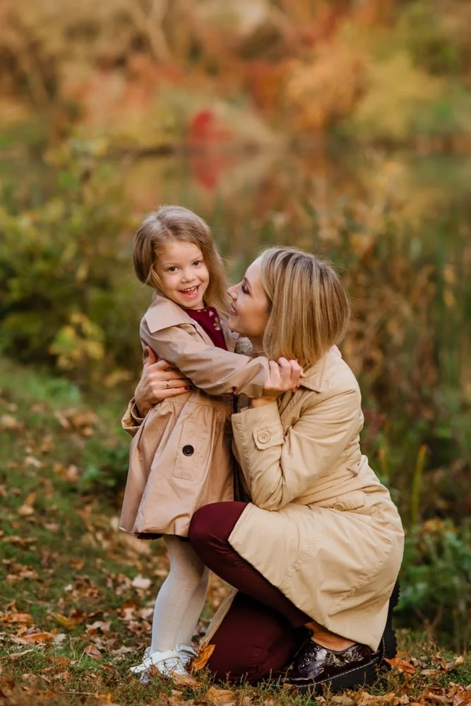 Eine Frau umarmt ein lachendes Mädchen im Herbstwald.