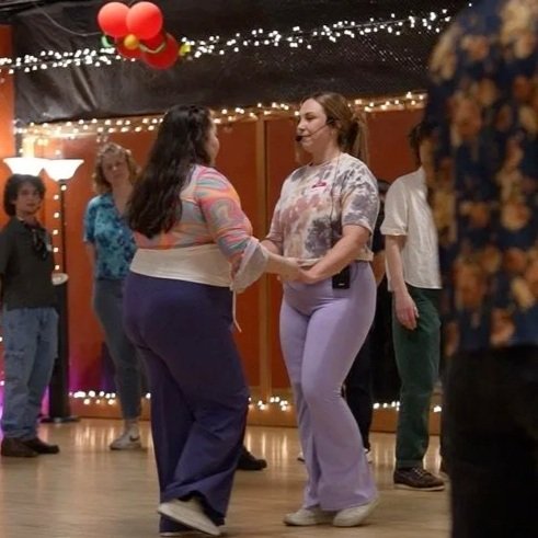 Two women dancing together at a social gathering with string lights and balloons in the background.