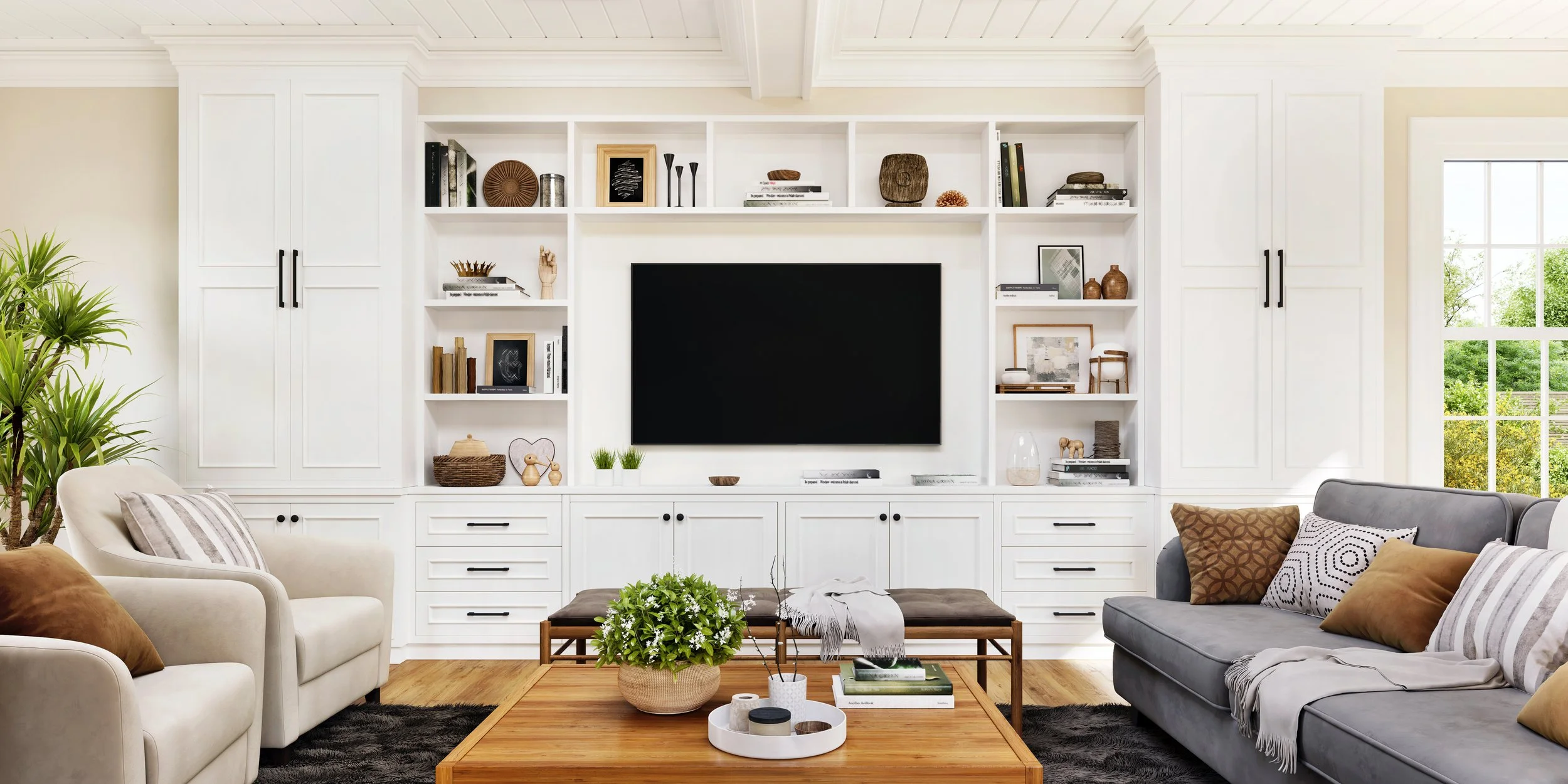 Living room with white built-in shelves, a central flat-screen TV, gray sofa with decorative pillows, cream armchair, coffee table with plants and books, hardwood floors, and a large window showing green trees outside.