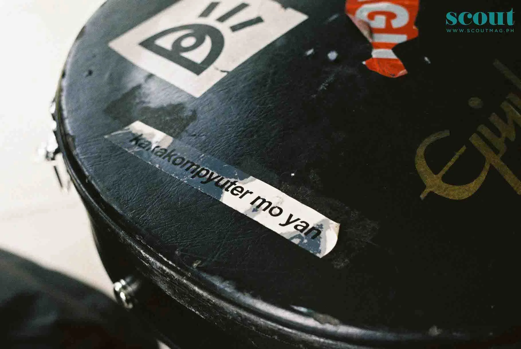 Close-up of a black surface with various stickers, including a partially visible sticker with the text 'Kakakompyuter Mo Yan'.