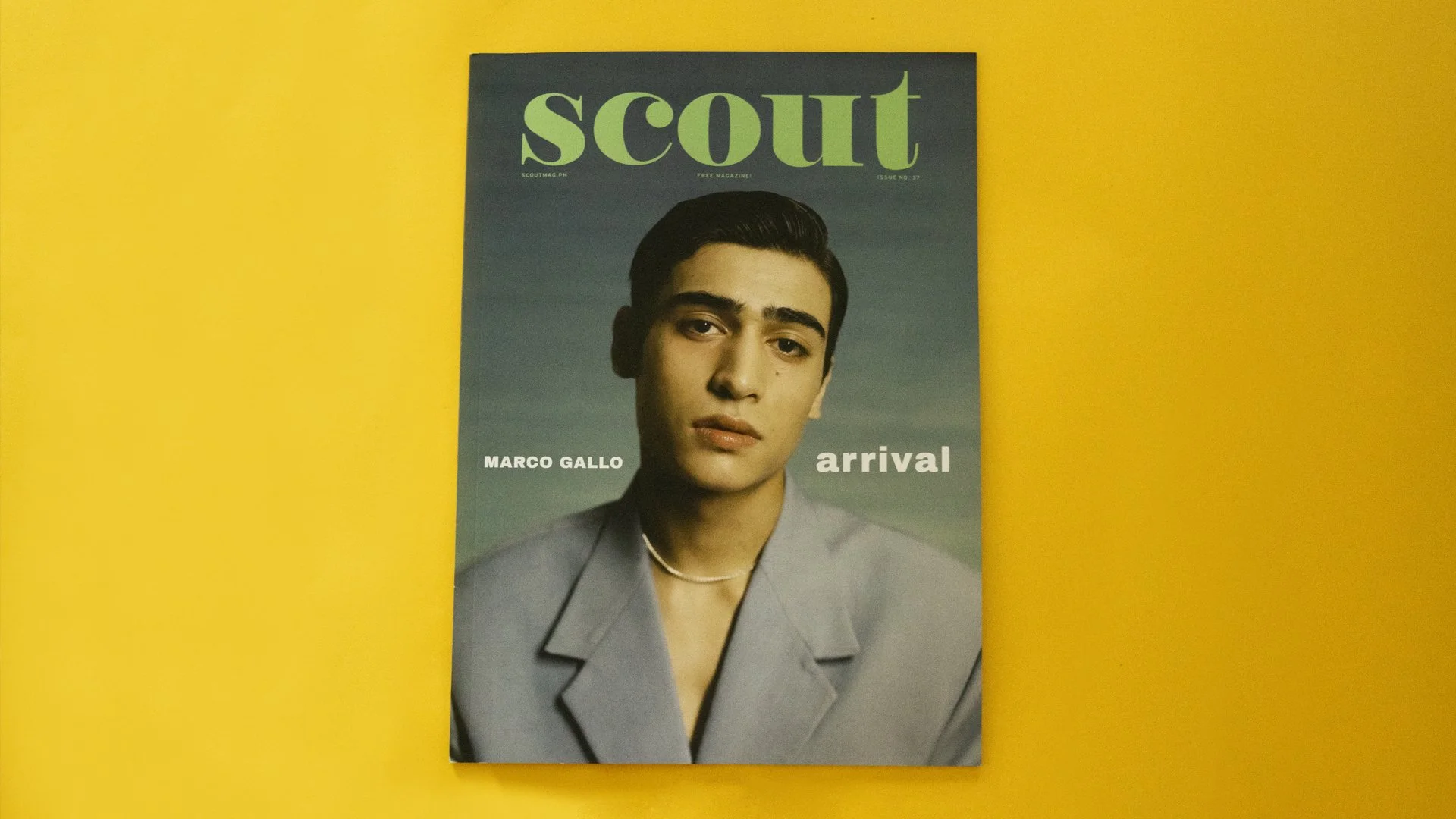 There is a magazine on a yellow background. The cover has a man looking at the viewer with the words, Marco Gallo and Arrival, on either side of him. Scout is above his head.