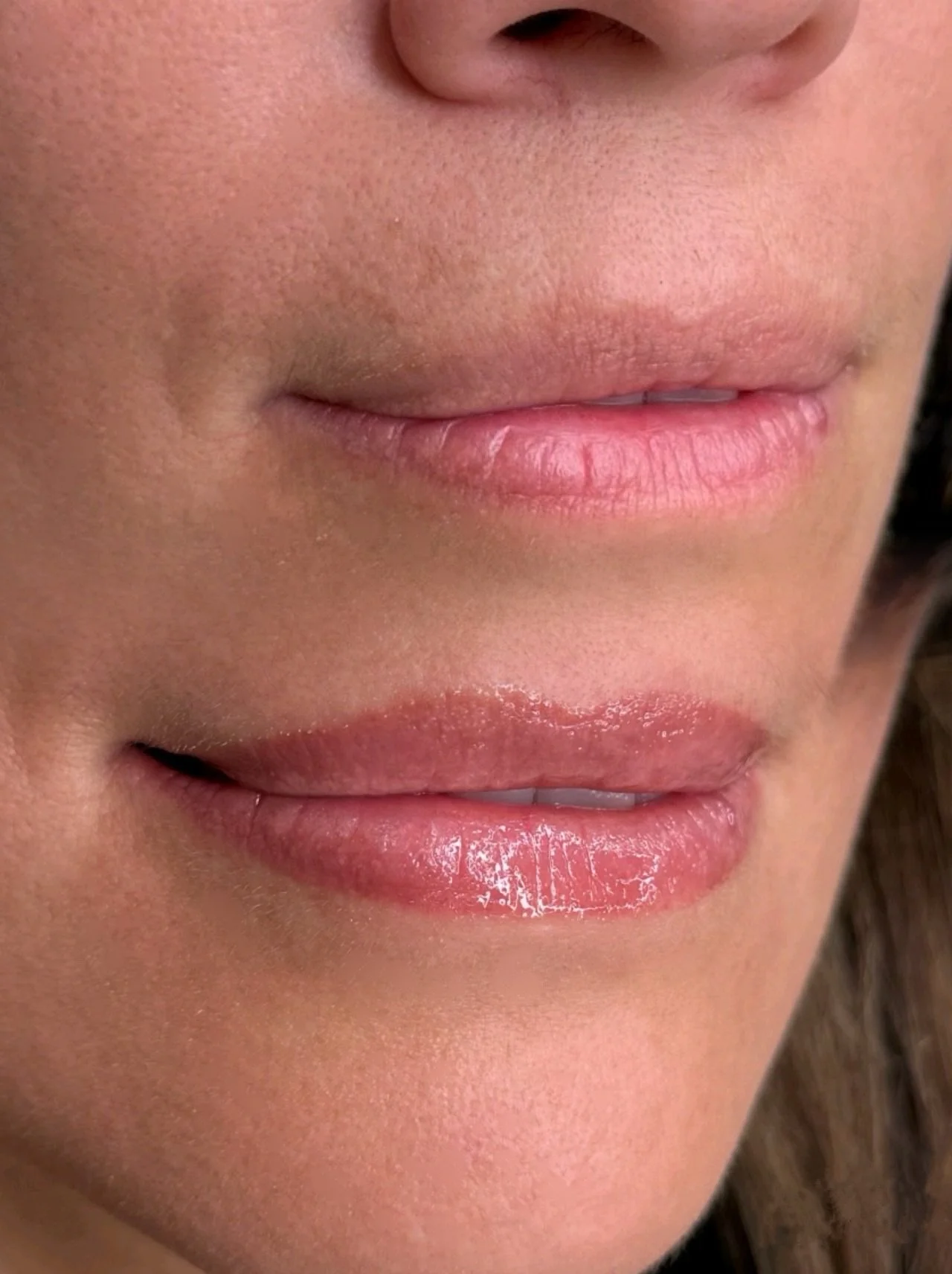 Close-up of a person's lips, with the upper lip lightly closed and the lower lip slightly parted, showing natural skin texture and lip gloss.
