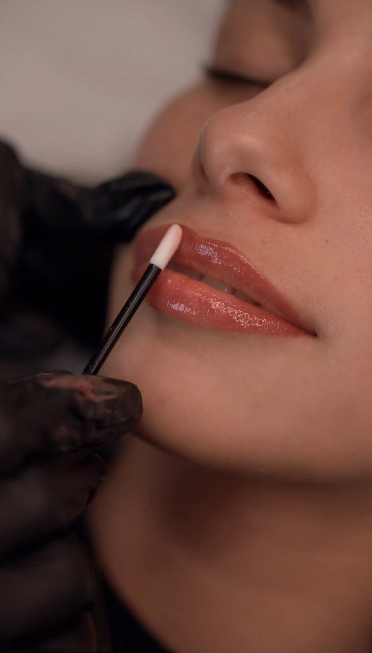 Person receiving lip makeup application with close-up shot of lips, nose, and makeup brush.