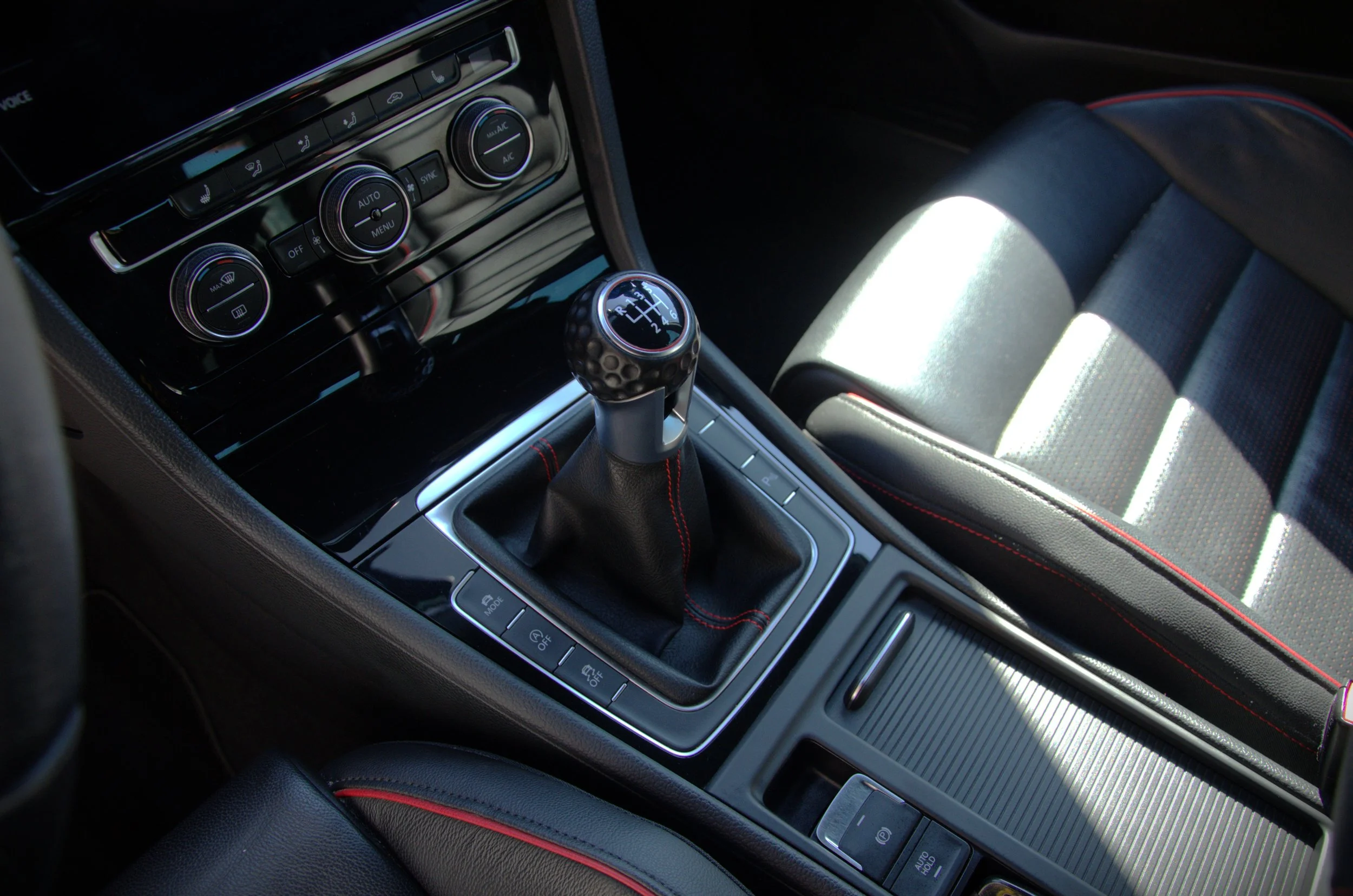 Interieur van een auto met een handgeschakelde versnellingspook en dashboardknoppen.
