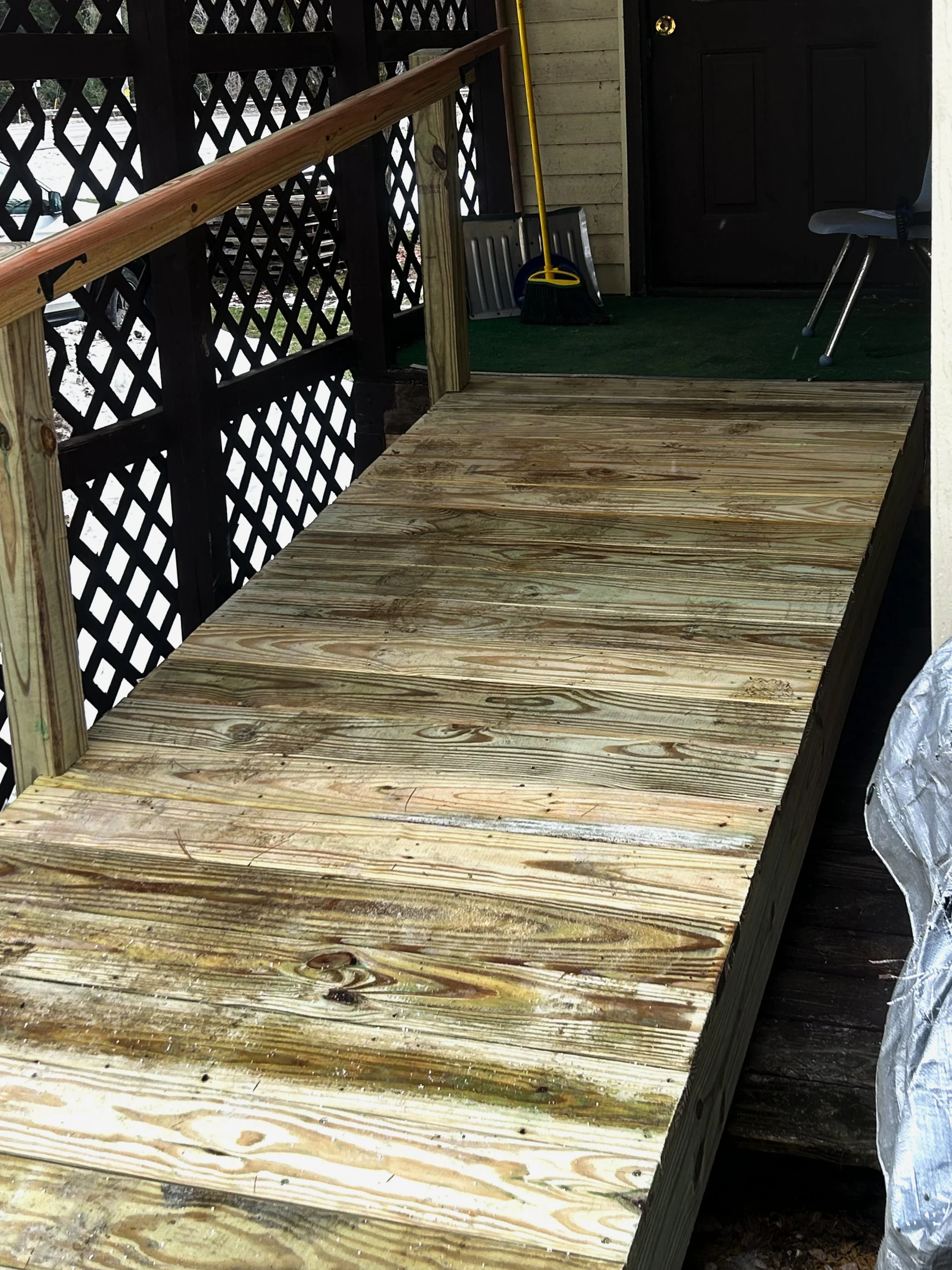 Wooden deck with a partial view of a porch area featuring cleaning tools and a small stool, enclosed by a lattice fence.
