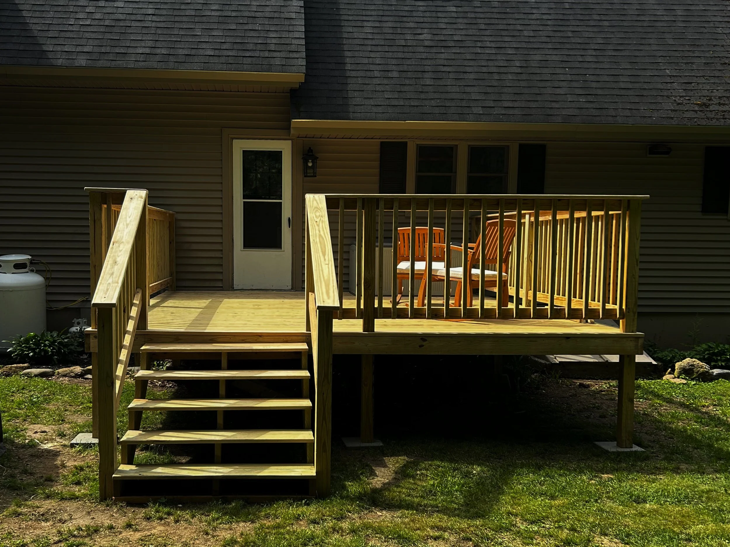 A newly constructed wooden deck with stairs and railing attached to the back of a house, with patio chairs on the deck.