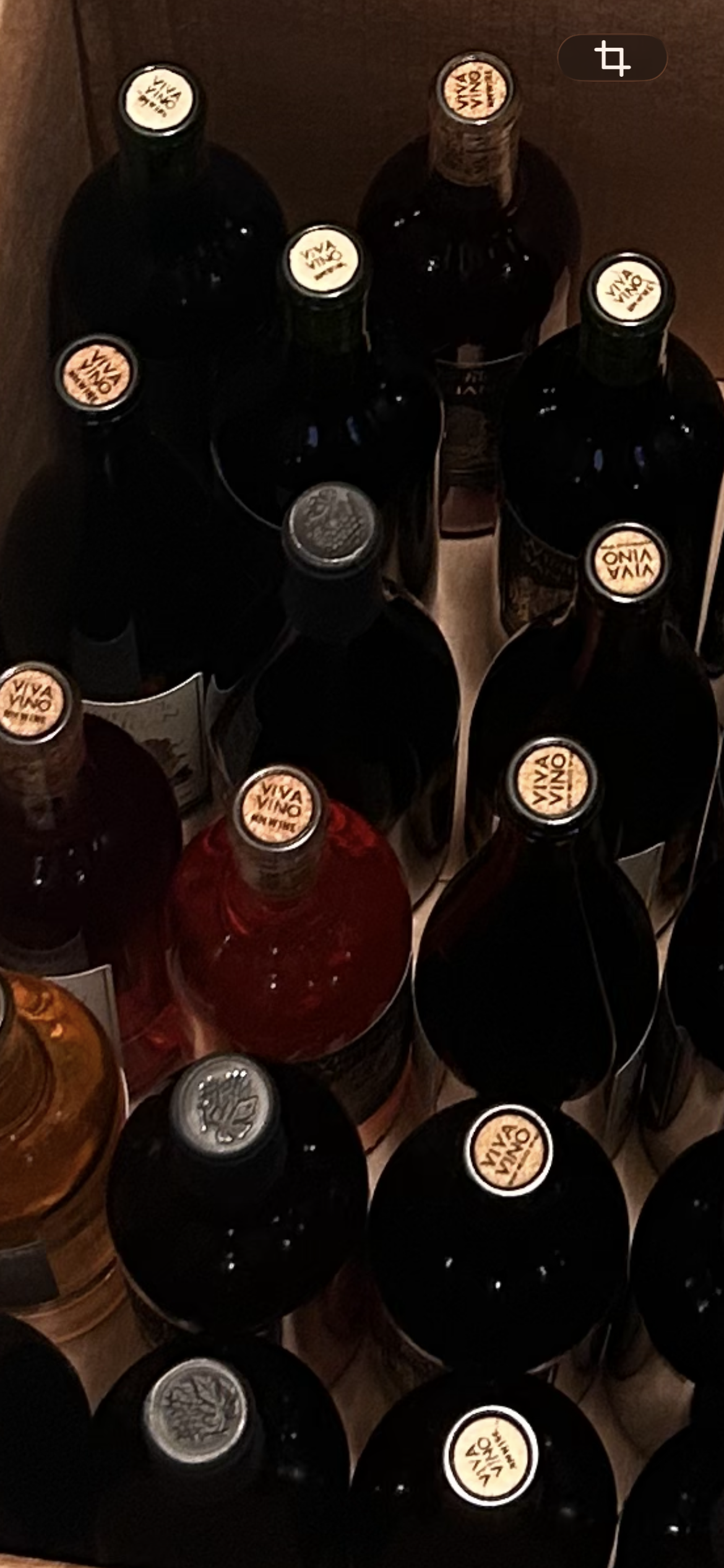 Top view of several wine bottles stored closely together in a wooden box, with visible corks and labels.