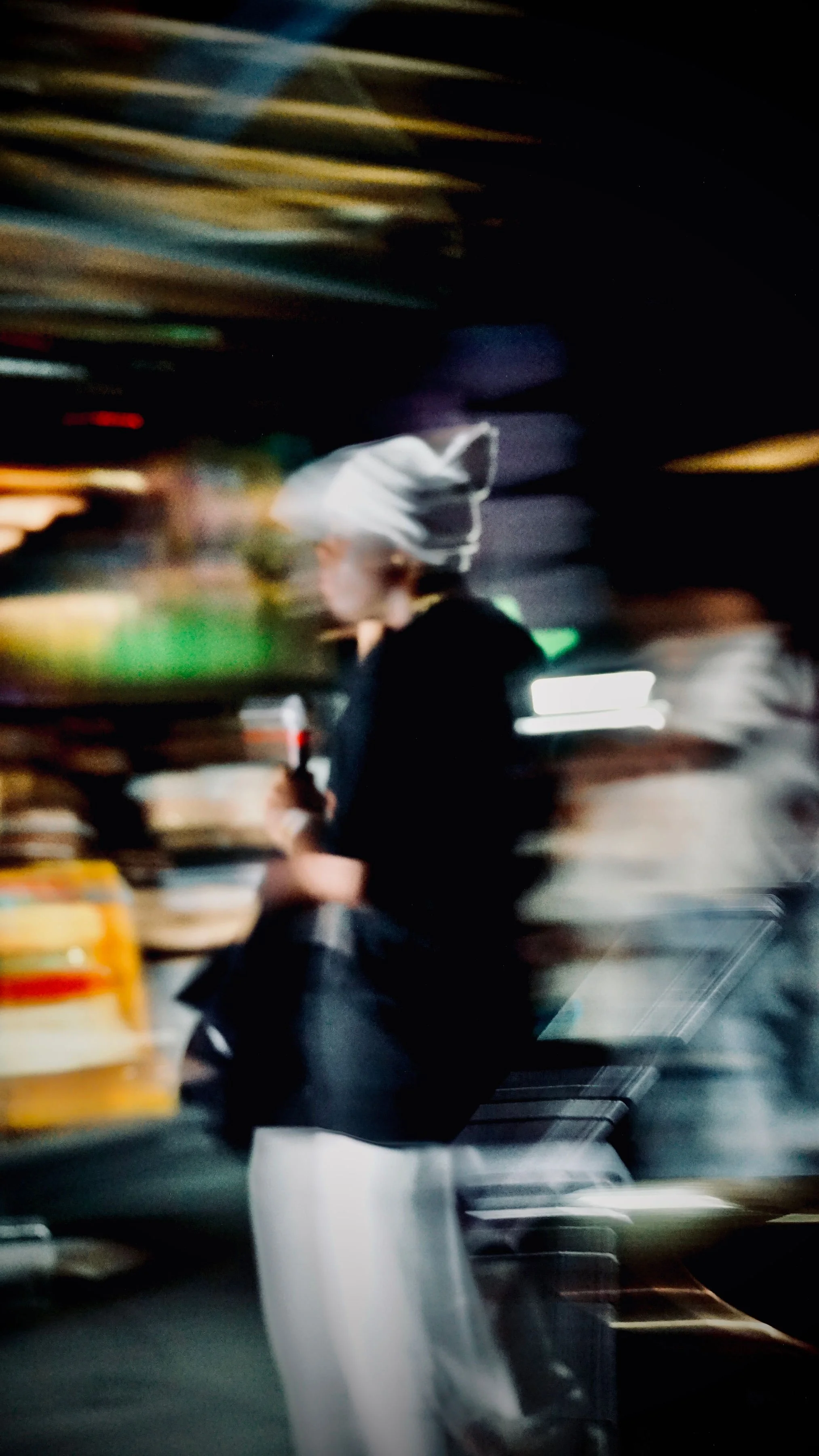 A person with a head covering and dark clothing holding a drink, captured with motion blur and set against a blurred background of a store or cafe.
