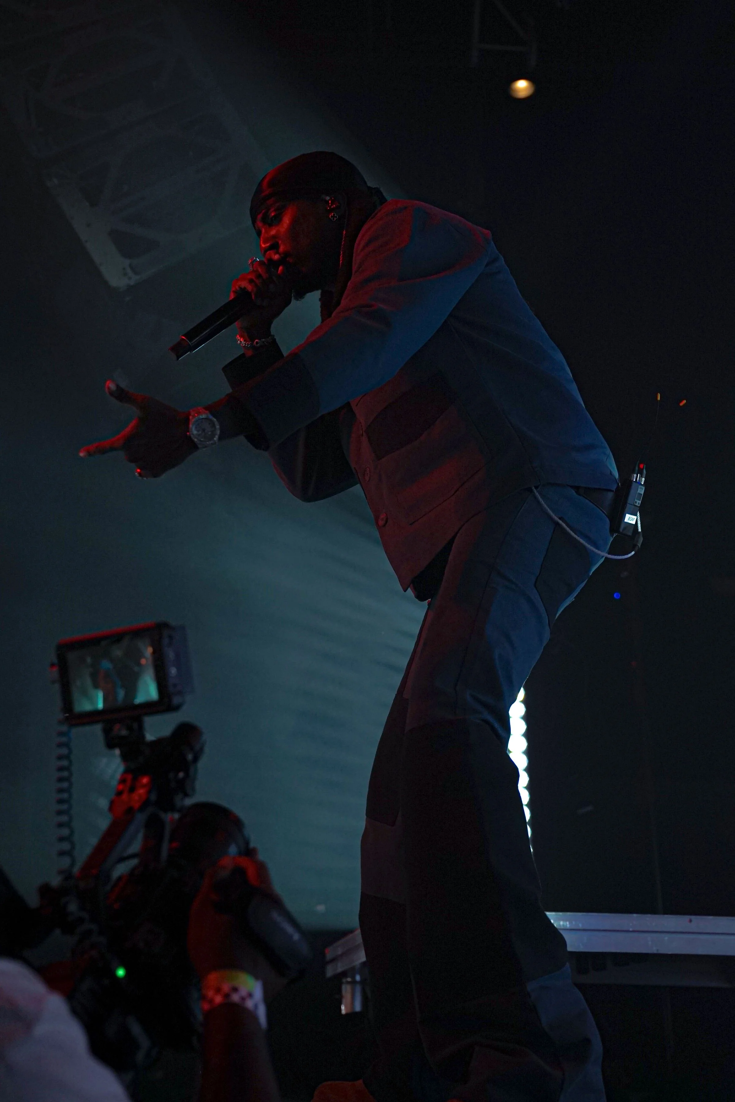 A male performer singing into a microphone on stage with stage lights and a camera filming him.