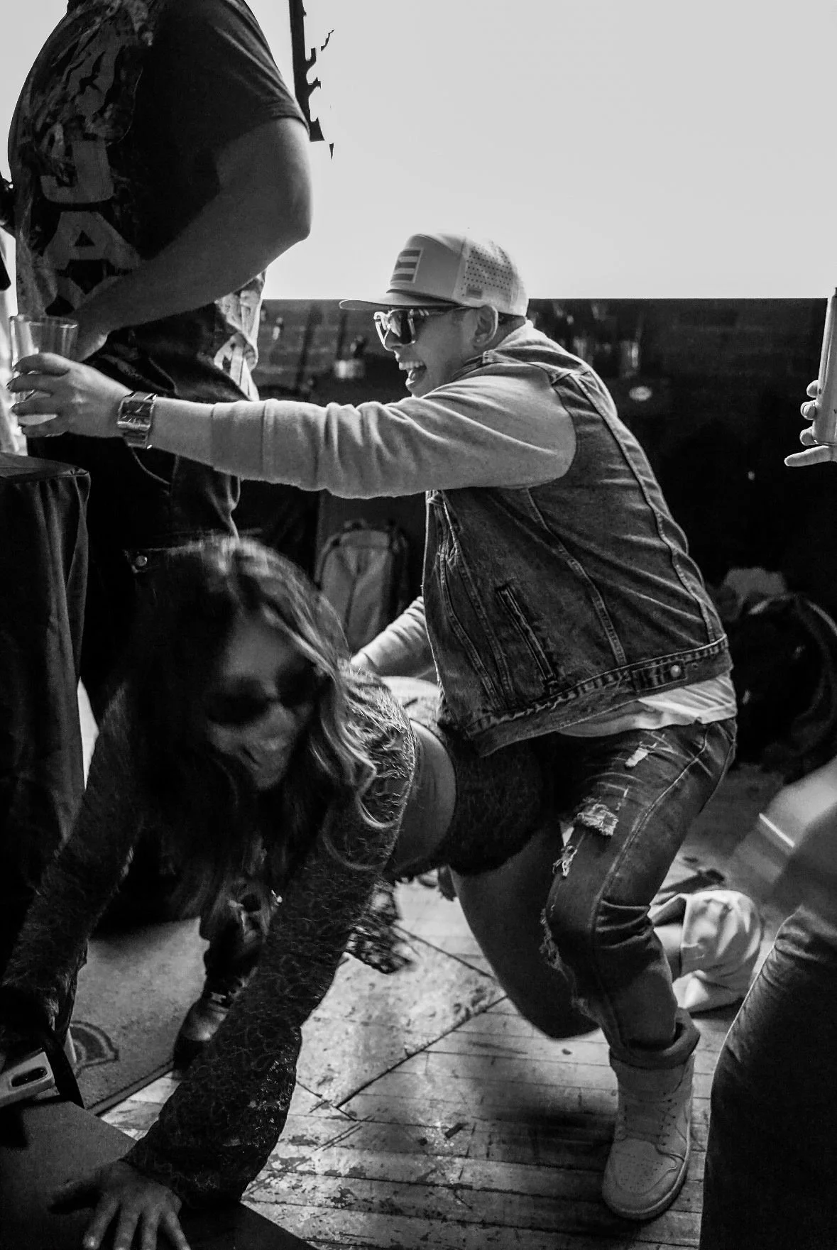 Two people inside a bar, one crouching on the floor and the other leaning over with a big smile, both holding drinks, in a lively and playful atmosphere.