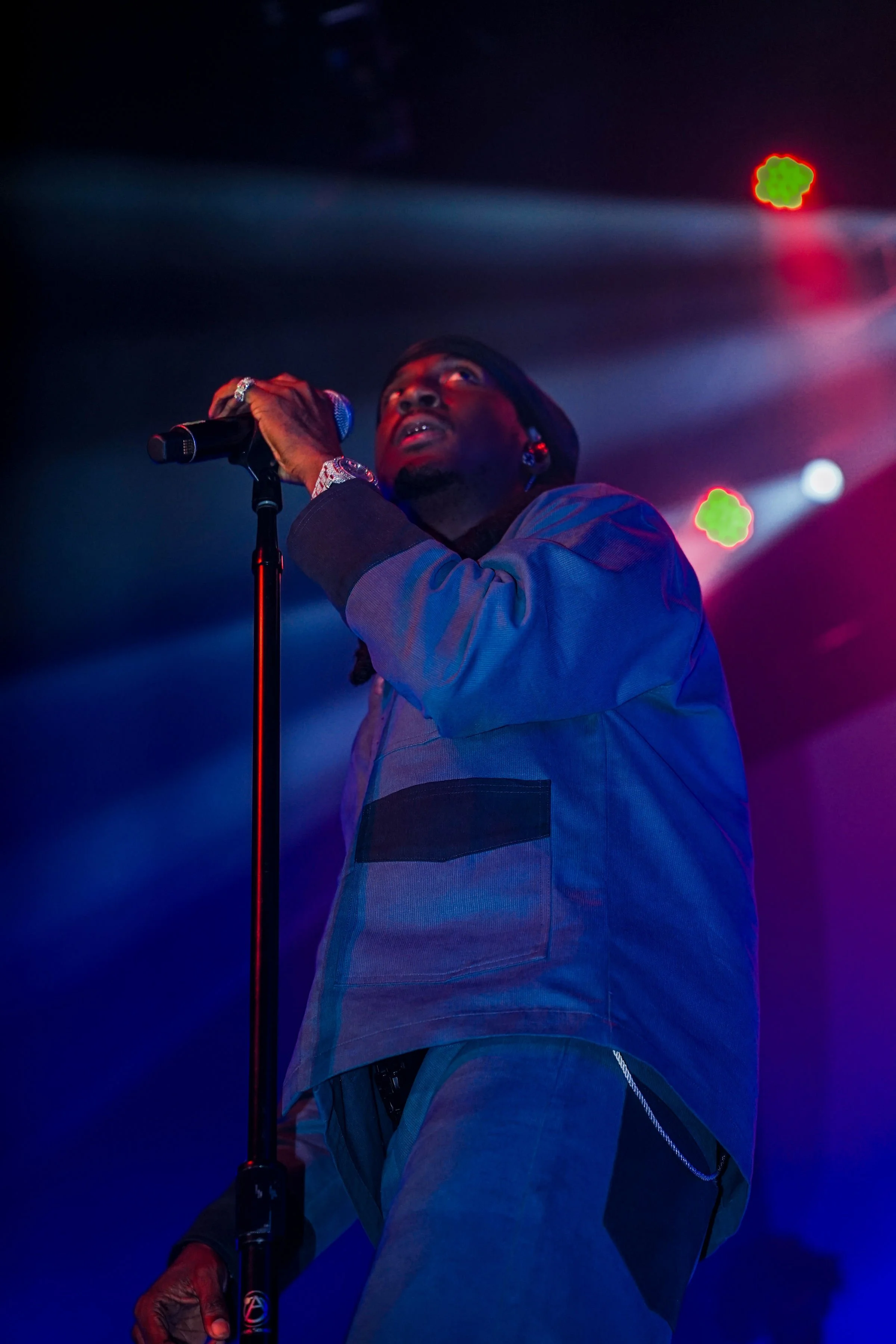 Performer on stage holding a microphone, illuminated by colorful stage lights.
