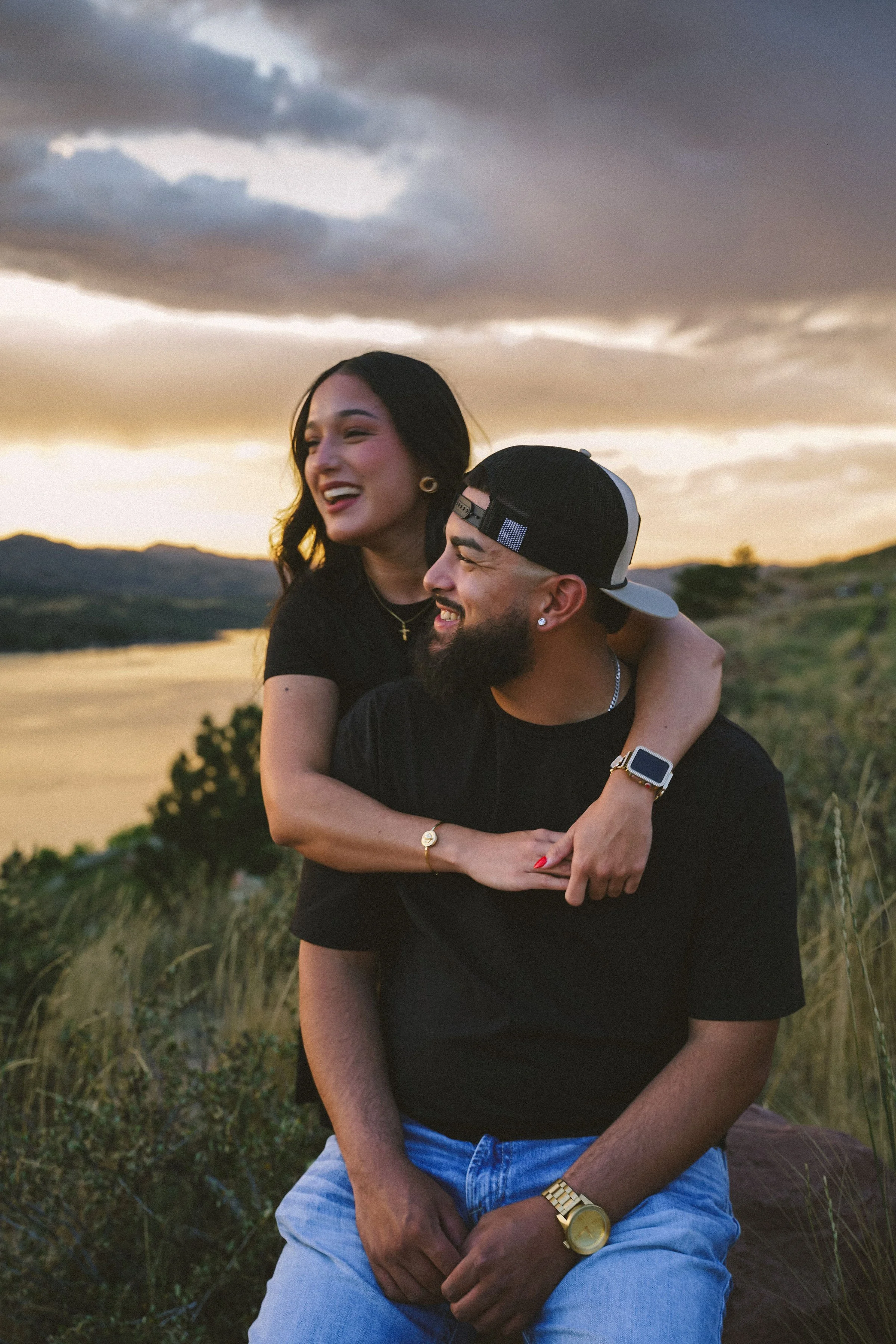 A happy couple outdoors at sunset, with the woman piggybacking on the man, both smiling and enjoying the moment.