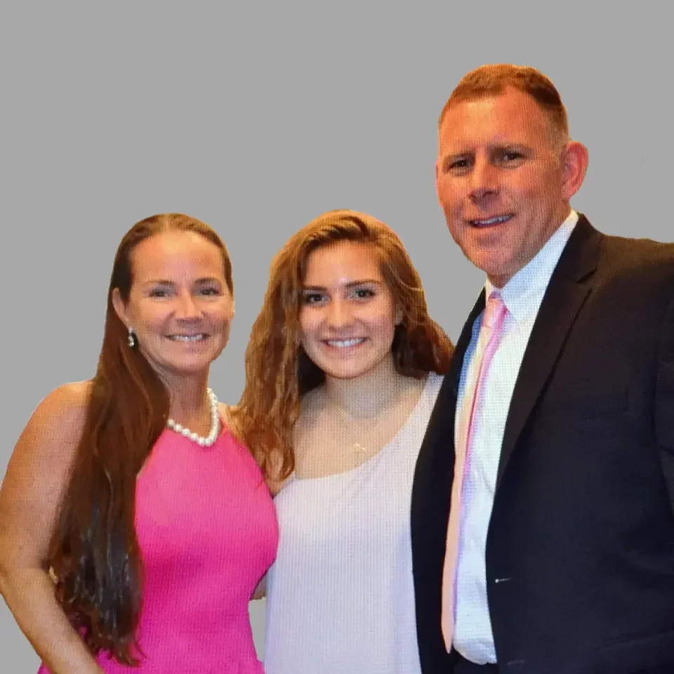 Three people, two women and one man, smiling and standing close together in front of a gray background, dressed semi-formally.