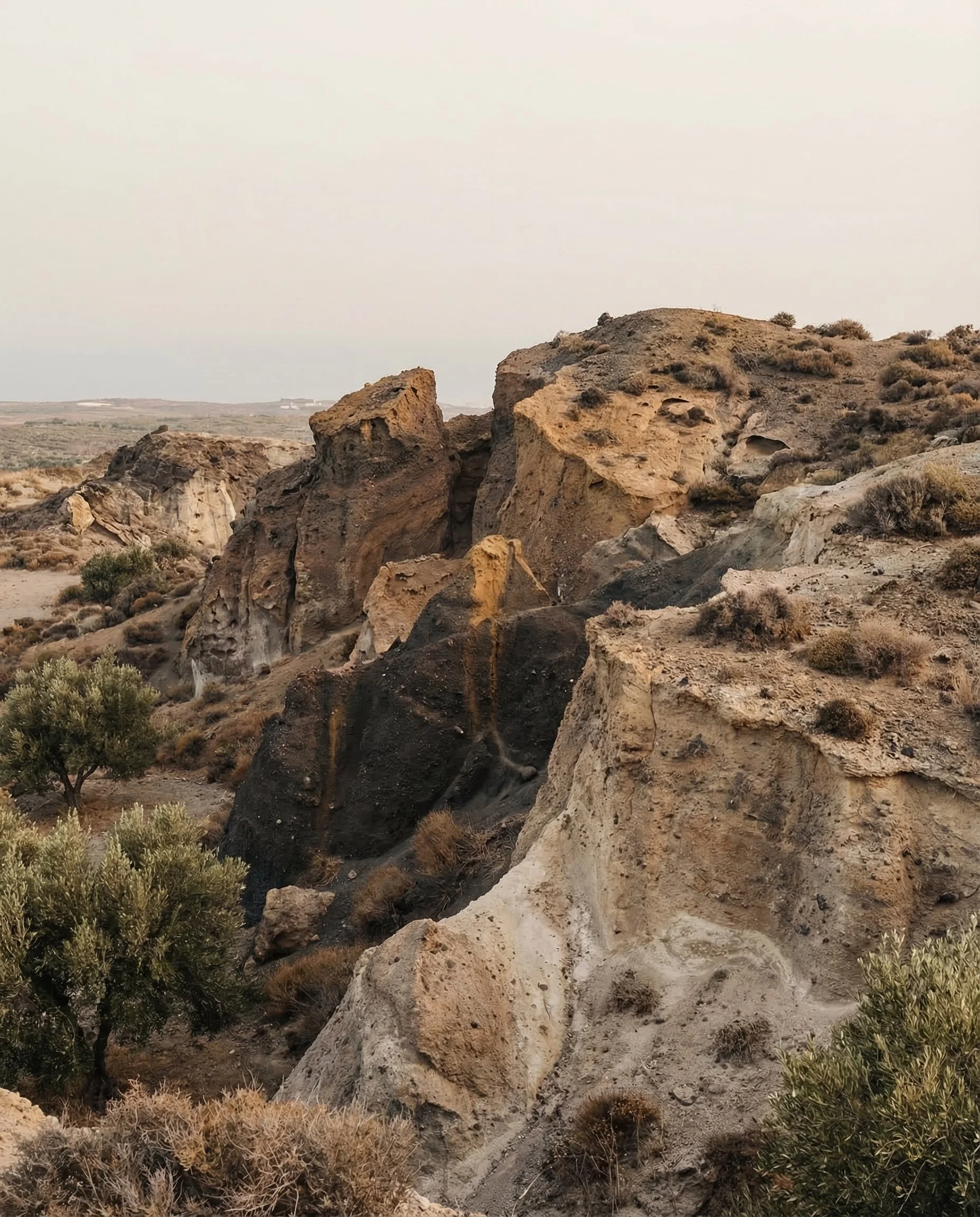 A rugged desert landscape with large, weathered rocks and sparse vegetation under a cloudy sky.