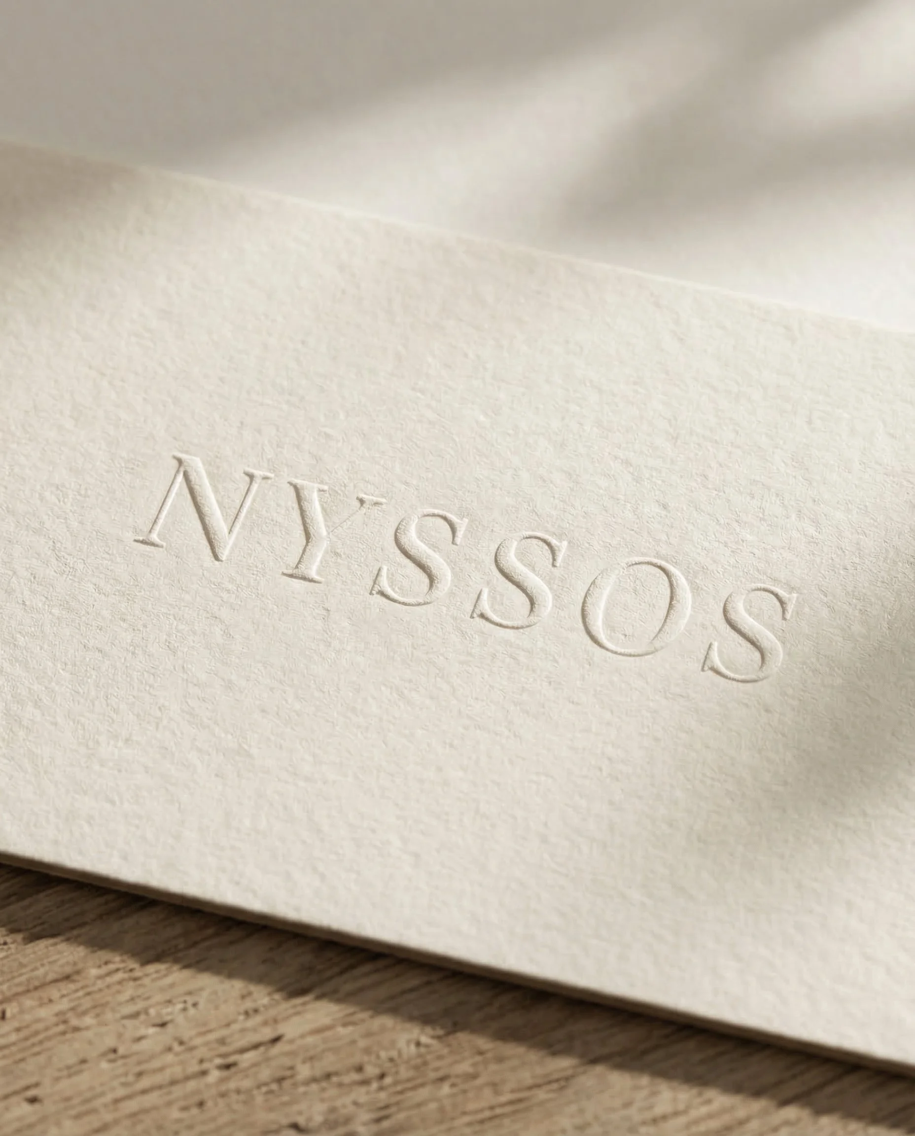 Close-up of embossed text on a cream-colored piece of paper that reads 'NYSSOS'.