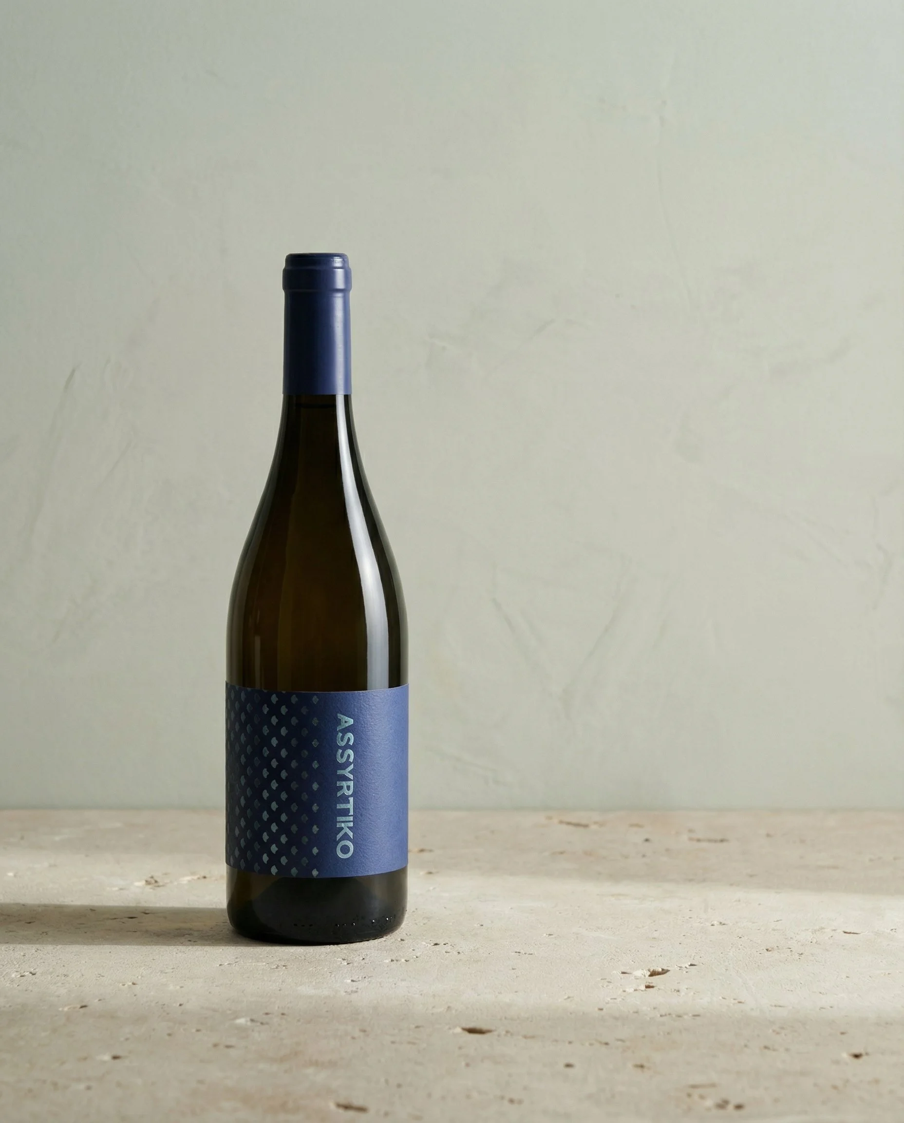 A bottle of wine with a blue label and matching blue capsule on the neck, placed on a light-colored wooden surface.