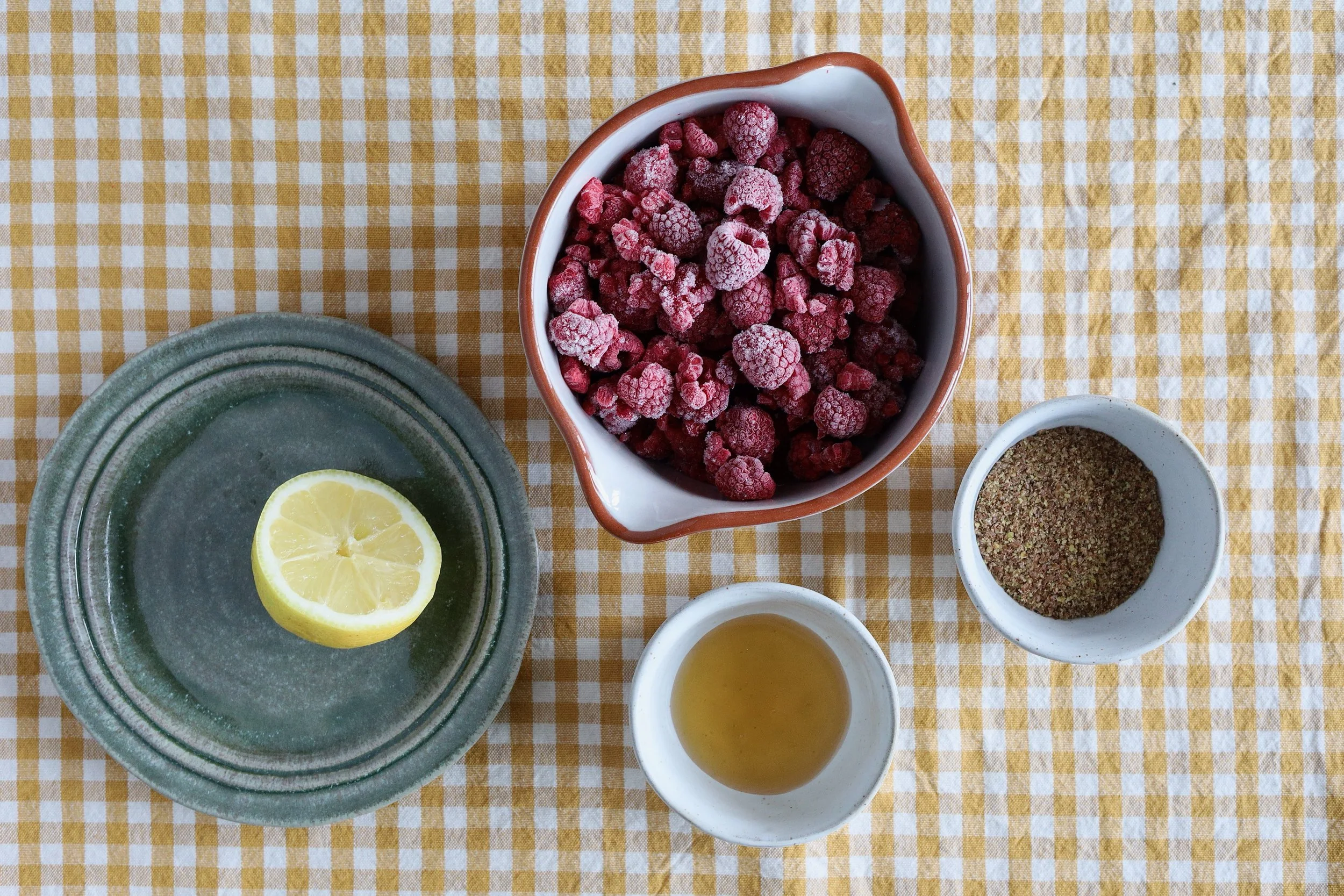 Schüssel mit Himbeeren neben kleineren Schälchen mit Honig und Leinsamen sowie einem Teller mit einer halben Zitrone
