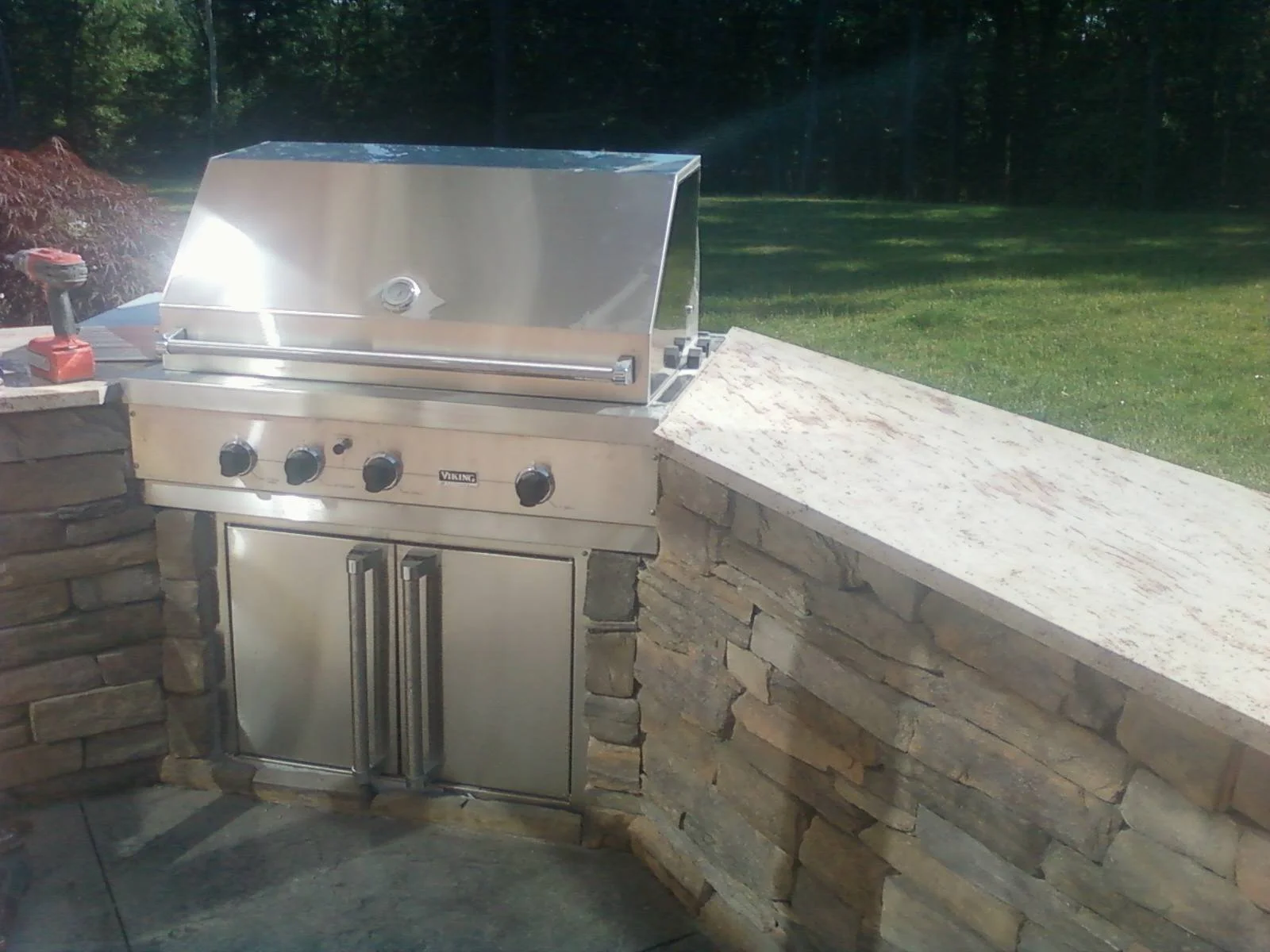 Outdoor stainless steel grill built into a stone countertop with a natural landscape background, masonry, desgin, colored stone