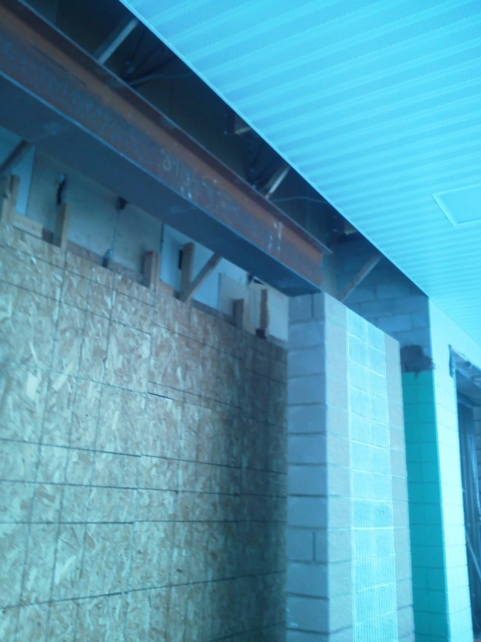 Construction site with metal beams, cinder blocks, and wooden framing, under a blue overhang or roof.