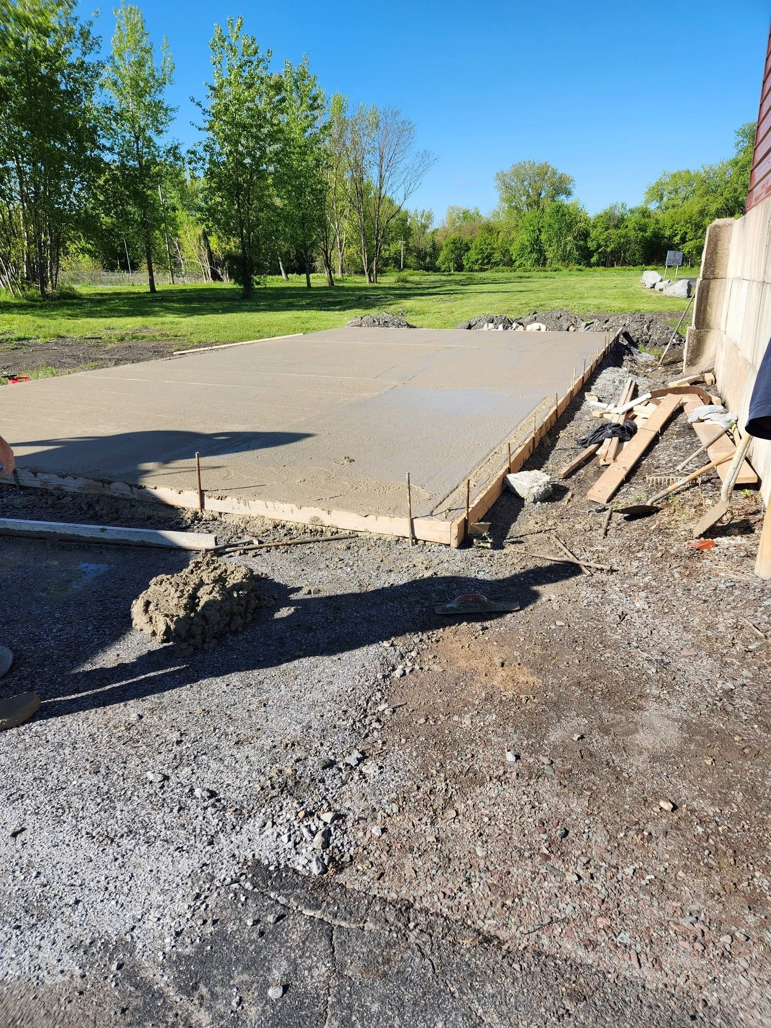 Construction site with freshly poured concrete slab, driveway, building slab, garage, equipment, storage