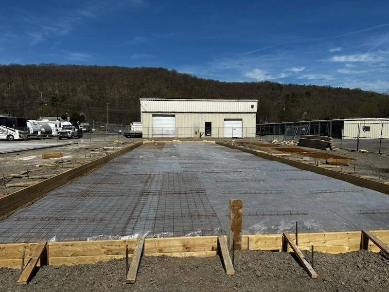 Construction site with concrete slab foundation and wooden forms with a warehouse, commercial, trucks, garage