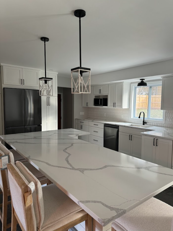 Modern kitchen with white cabinets, large island with white and gray marble countertop, black appliances, and two pendant light fixtures.