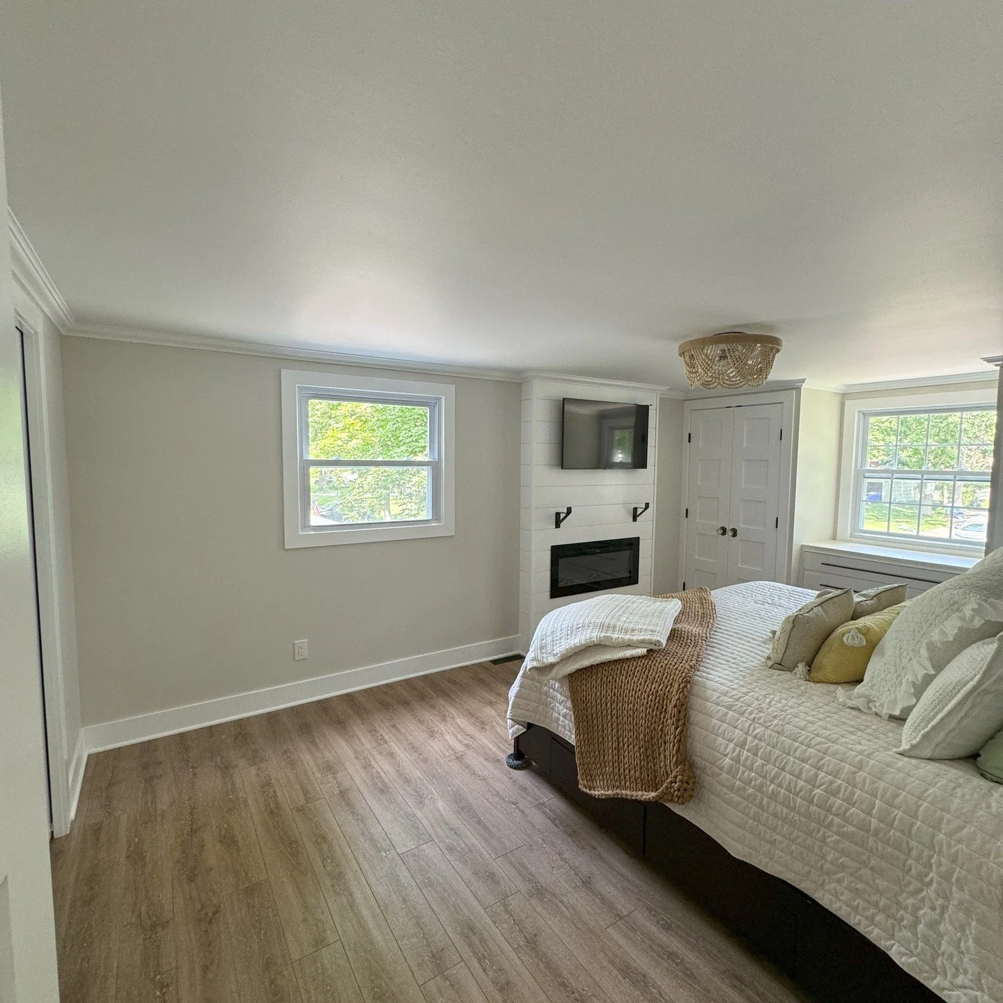 A modern bedroom with a bed, window, mounted TV, and hardwood floors.