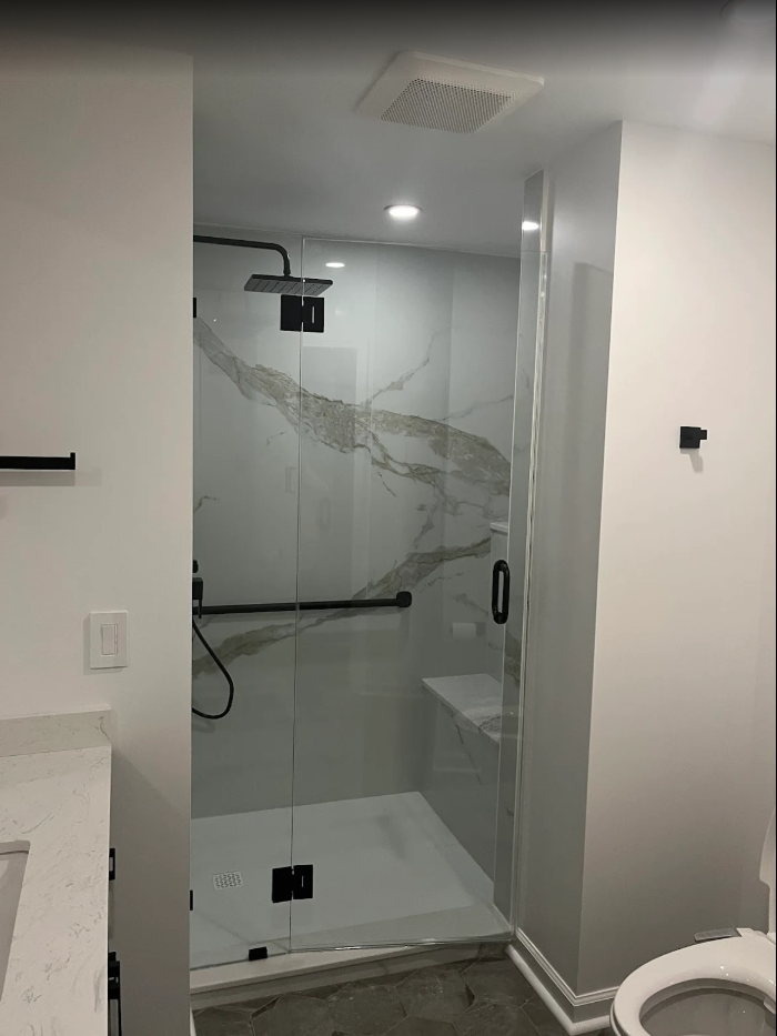 Modern glass-enclosed shower with marble accent wall and bench, black fixtures, and a rain showerhead.
